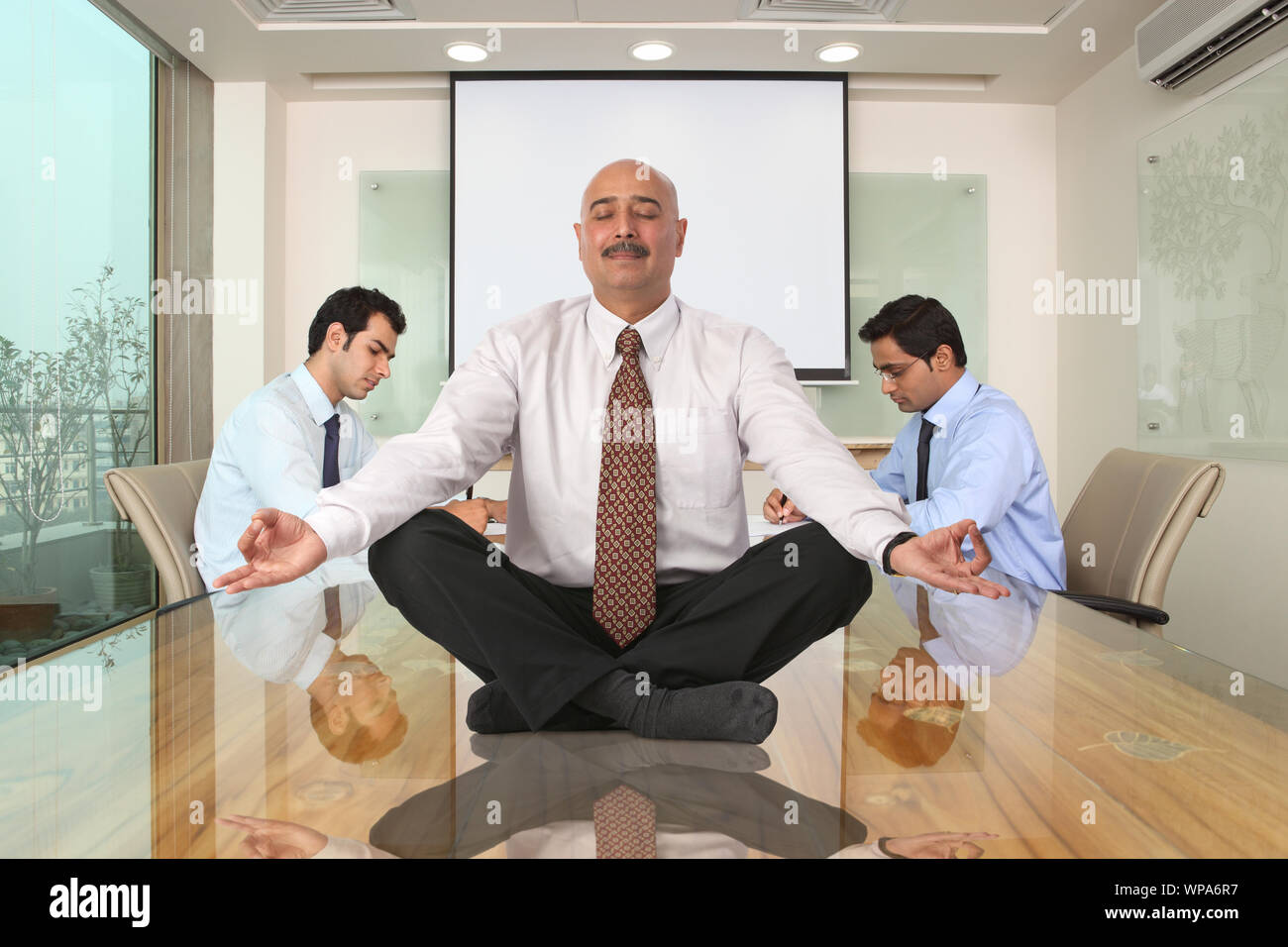 Geschäftsmann sitzt in Yoga-Pose auf dem Tisch Stockfoto