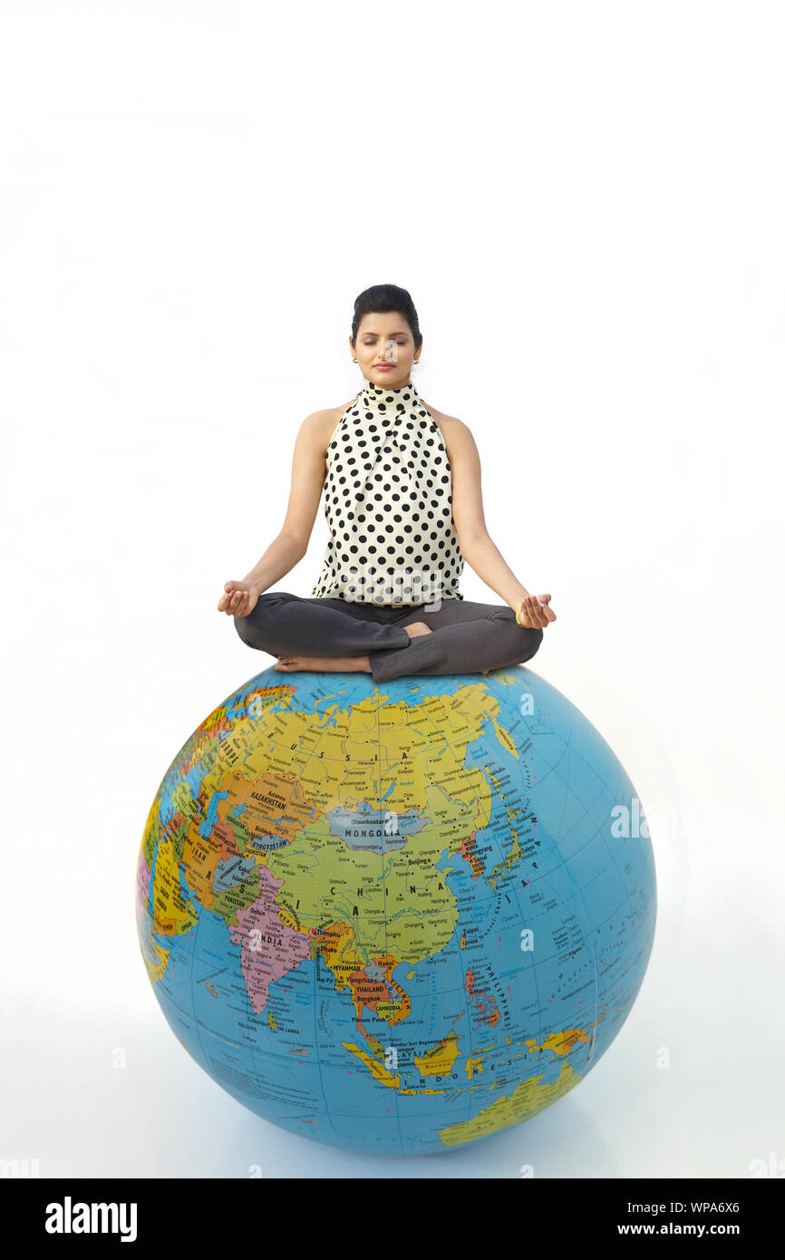 Geschäftsfrau, die in Yoga-Pose auf einem Globus sitzt Stockfoto