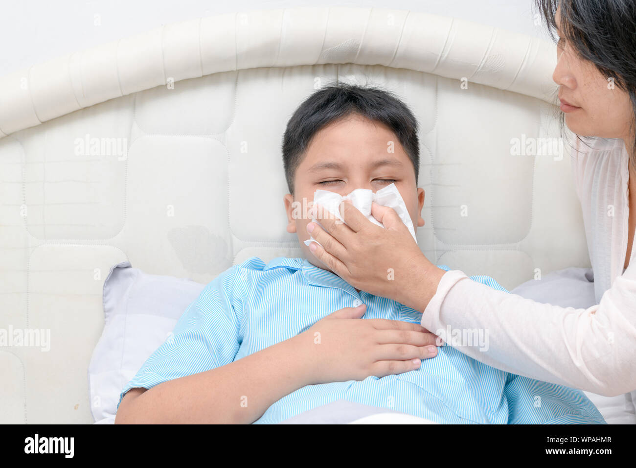 Sick asiatische Kind wischen oder Reinigung der Nase mit einem Taschentuch, während die Mutter ihm zu helfen. Health Care, Fieber und Grippe Konzept. Stockfoto