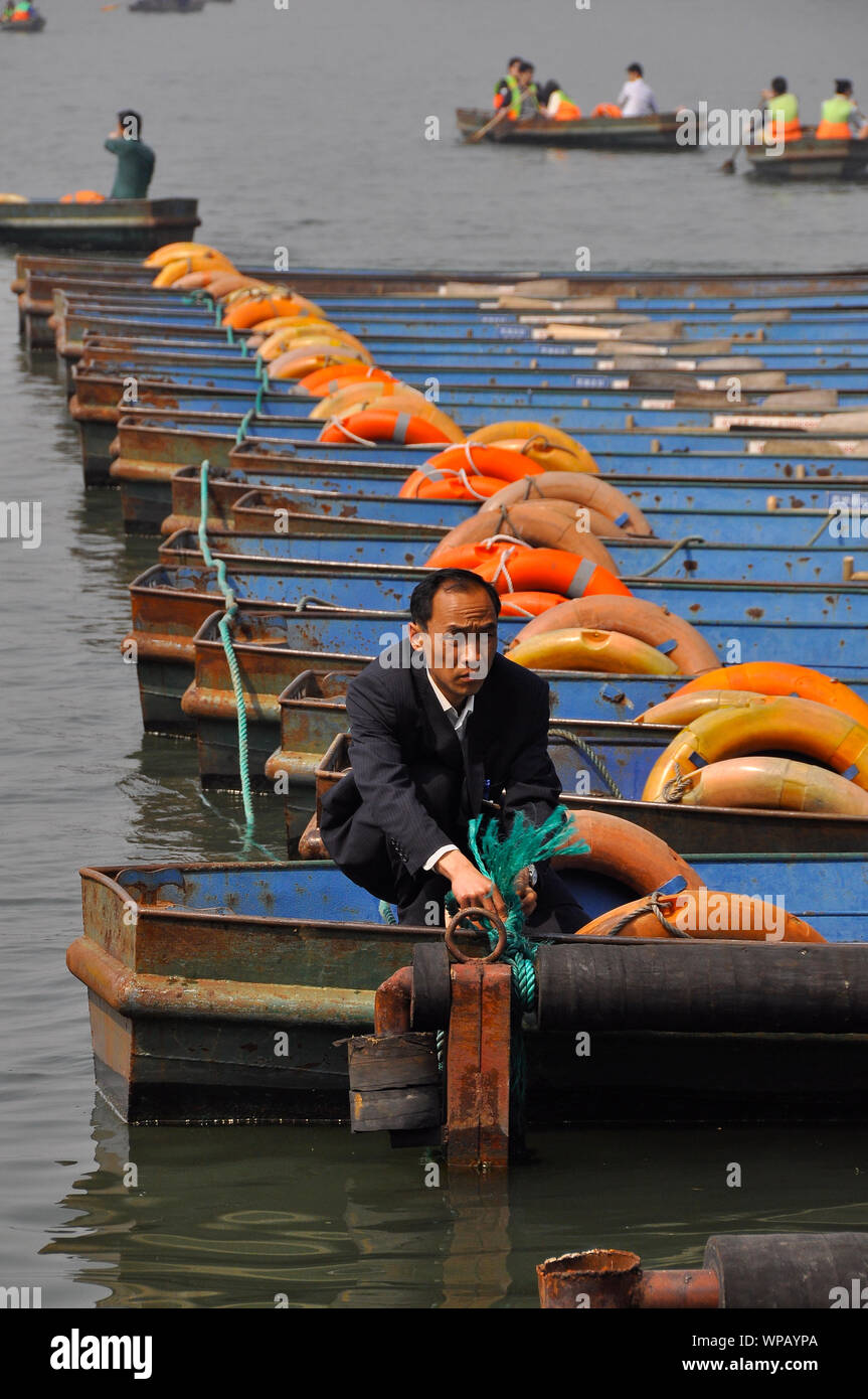 Ein chinesischer Mann sichert seine touristische Ruderboote auf dem See an der Huangzhou Stockfoto