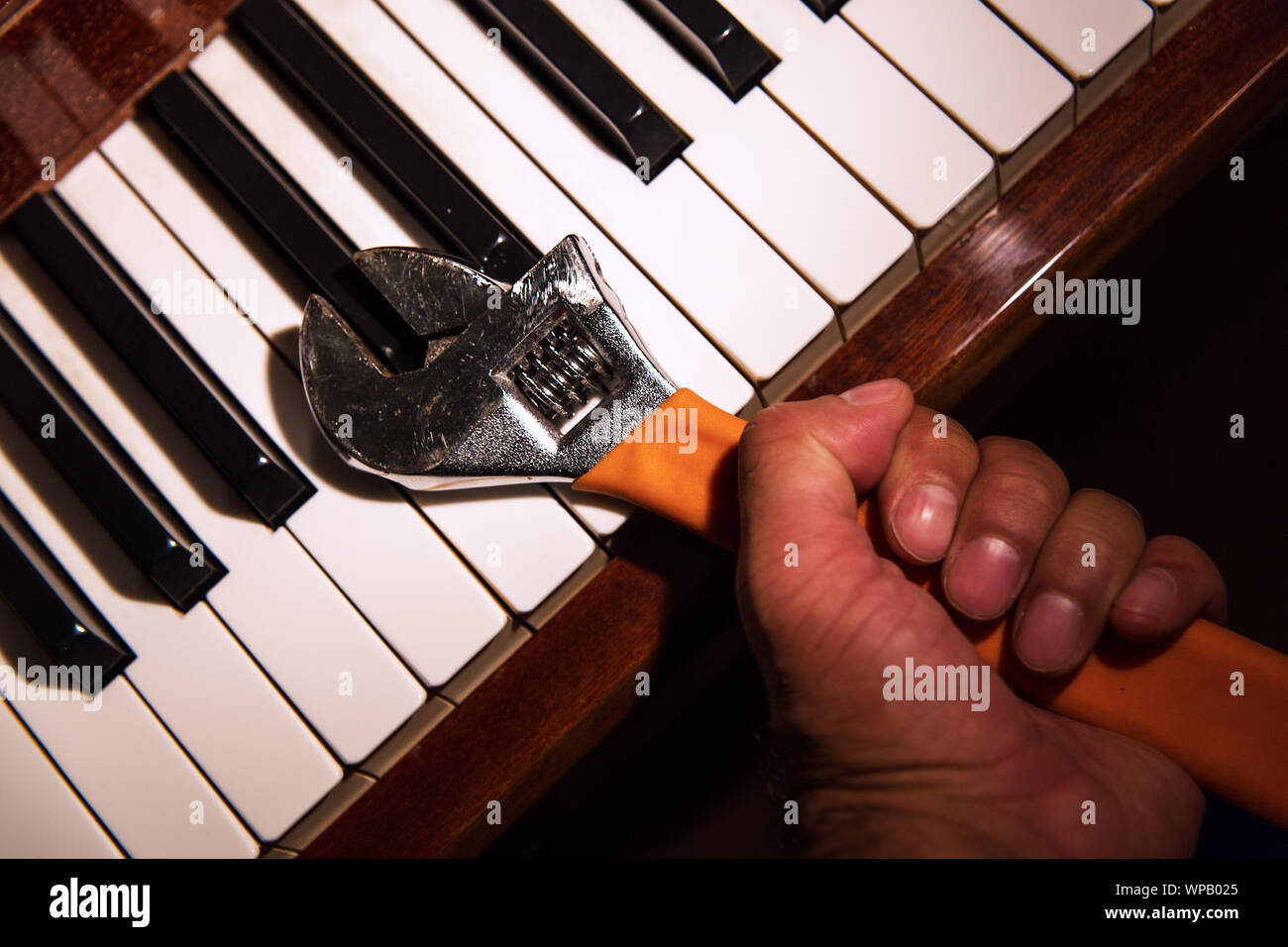 Nahaufnahme, Ansicht von oben auf die Hand eines Mannes Holding einen verstellbaren Schraubenschlüssel, einer der Schlüssel eines klassischen Piano Holding. Die Misshandlung von Musikinstrumenten. Stockfoto