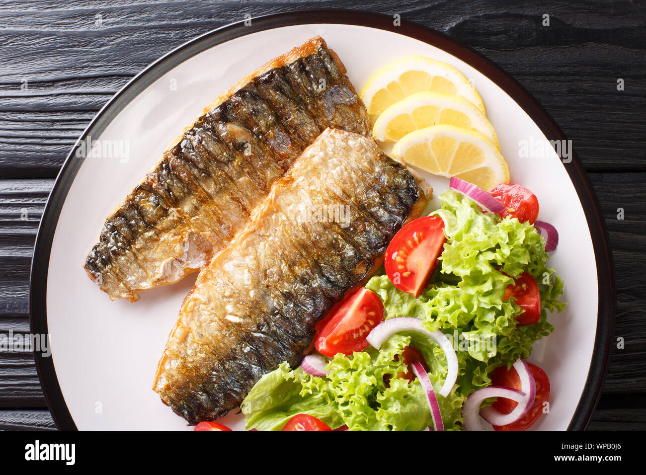 Teil der gegrillte Makrelen Filet mit Zitrone und frischen Salat close-up auf einem Teller auf den Tisch. Horizontal oben Ansicht von oben Stockfoto
