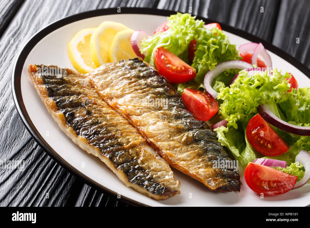 Teil der gegrillte Makrelen Filet mit Zitrone und frischen Salat close-up auf einem Teller auf den Tisch. Horizontale Stockfoto