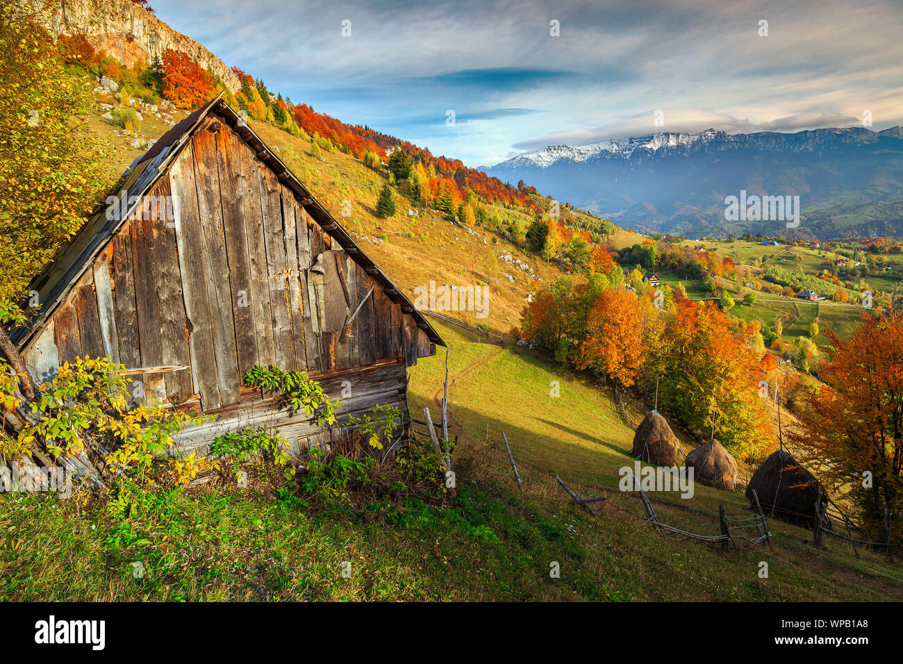 Fantastische Herbst alpine Landschaft, Alpine Village mit Klapprige Holzhütte und hohen schneebedeckten Berge im Hintergrund in der Nähe von Brasov, Magura, Siebenbürgen, Ro Stockfoto