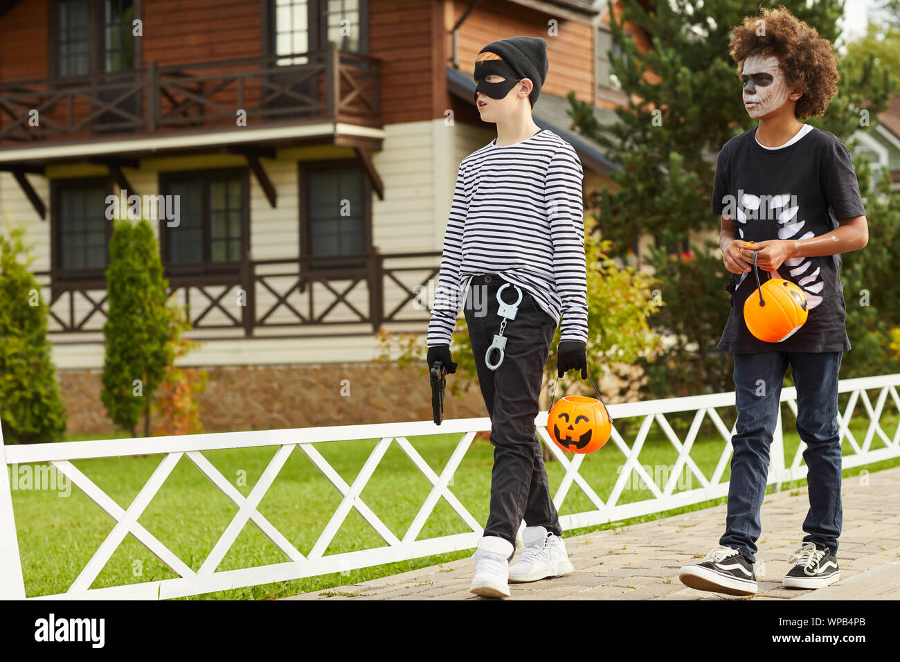 In voller Länge Porträt von zwei Jungen im Teenageralter tragen Halloween Kostüme Walking im Freien in der Straße während Trick oder das Behandeln mit Kürbis Körbe, Kopie Raum Stockfoto