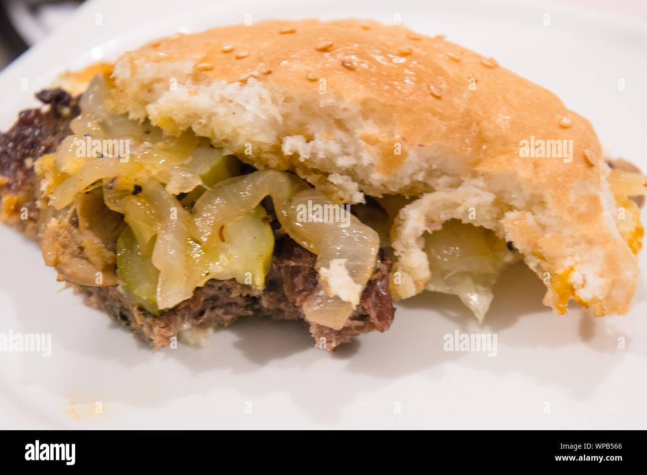 Die Hälfte gegessen Sesamsamen abgedeckt burger Brötchen mit saftigen Patty und lecker Zwiebeln und Gurken Stockfoto