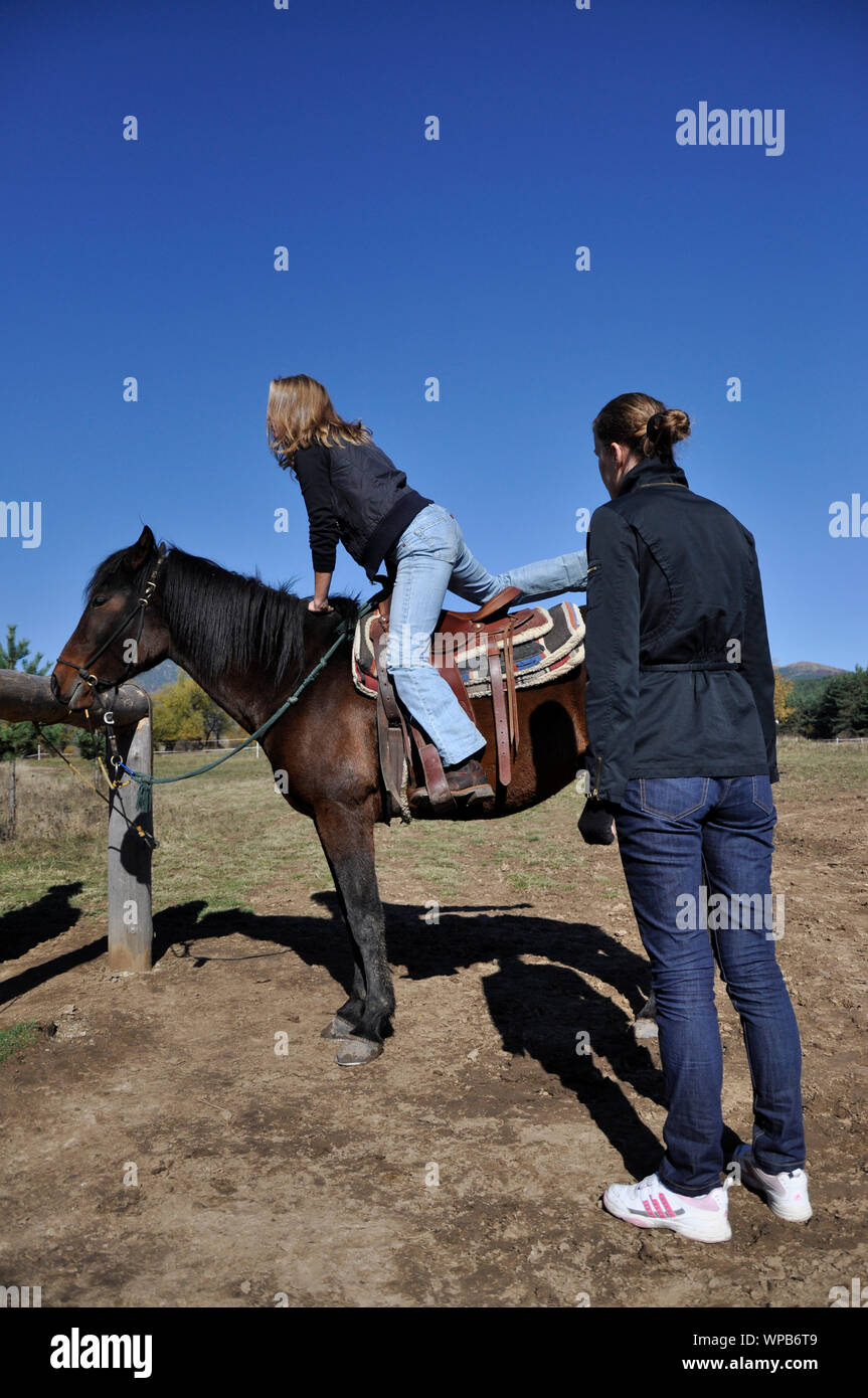 Tag auf der Ranch. Professionelle Pferd Reiter zeigt eine junge Frau wie auf einem Pferd zu erhalten. Stockfoto
