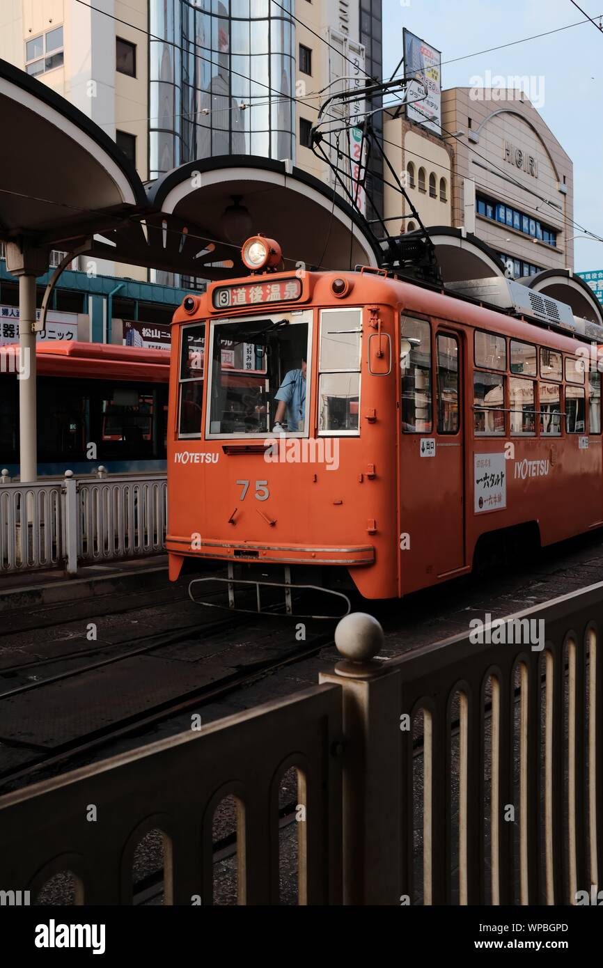 MATSUYAMA, Japan - 04.August 2019: Eine vertikale Schuß eines Roten Zug auf einer Schiene an einem Bahnhof in der Nähe von Gebäuden Stockfoto