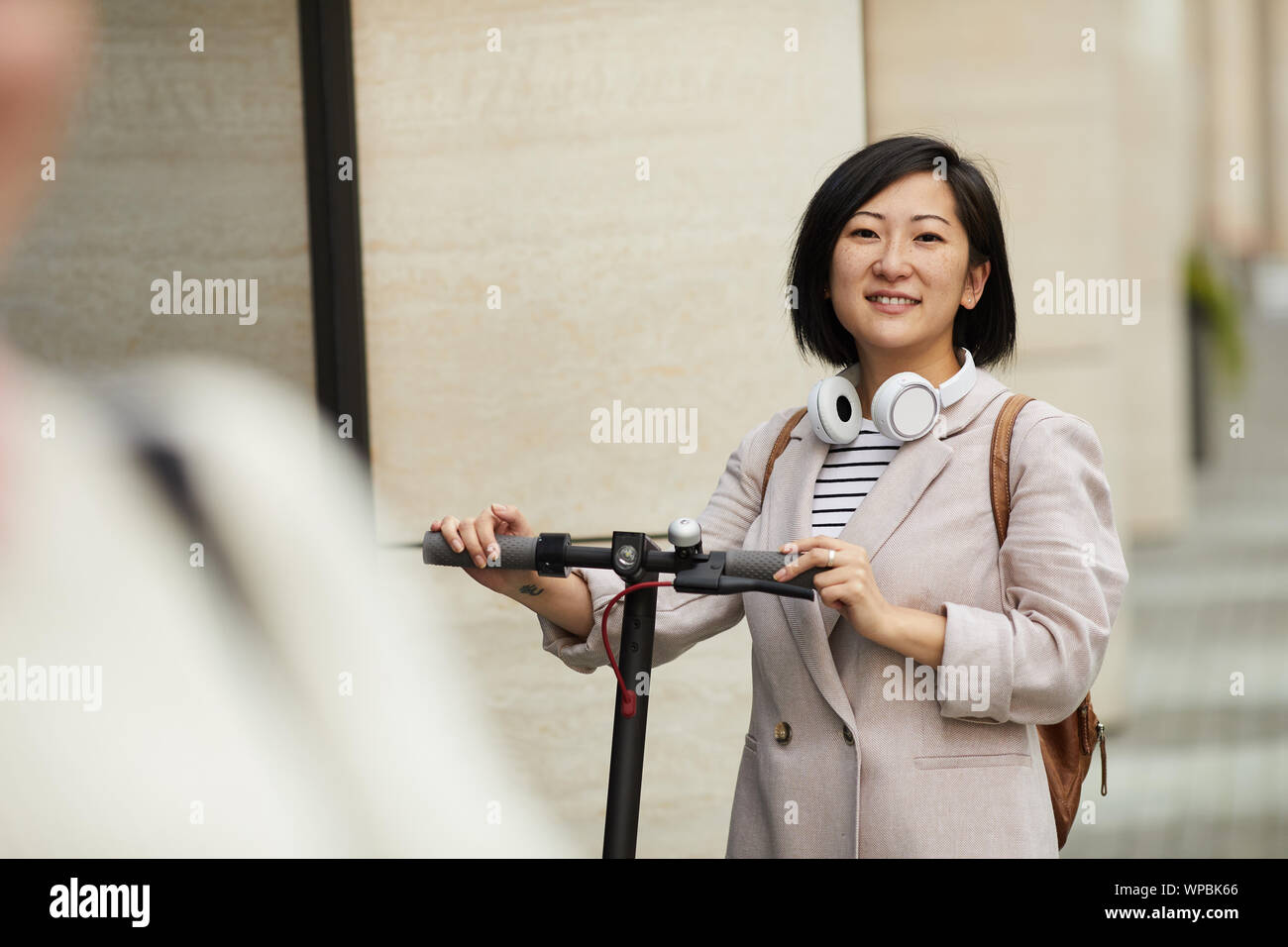 Taille bis Portrait von jungen asiatischen Frau, Elektroroller und Suchen an der Kamera, während draußen in der Stadt Straße Posing, kopieren Raum Stockfoto