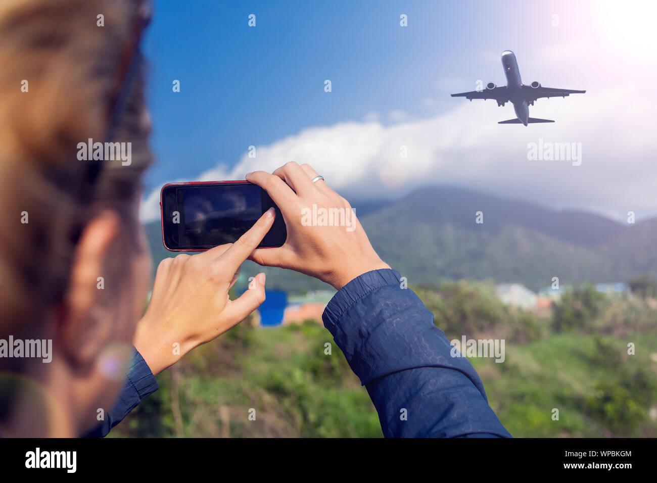 Frau macht Foto von dem Flugzeug am Himmel über den Bergen. Urlaub und Reisen Konzept Stockfoto