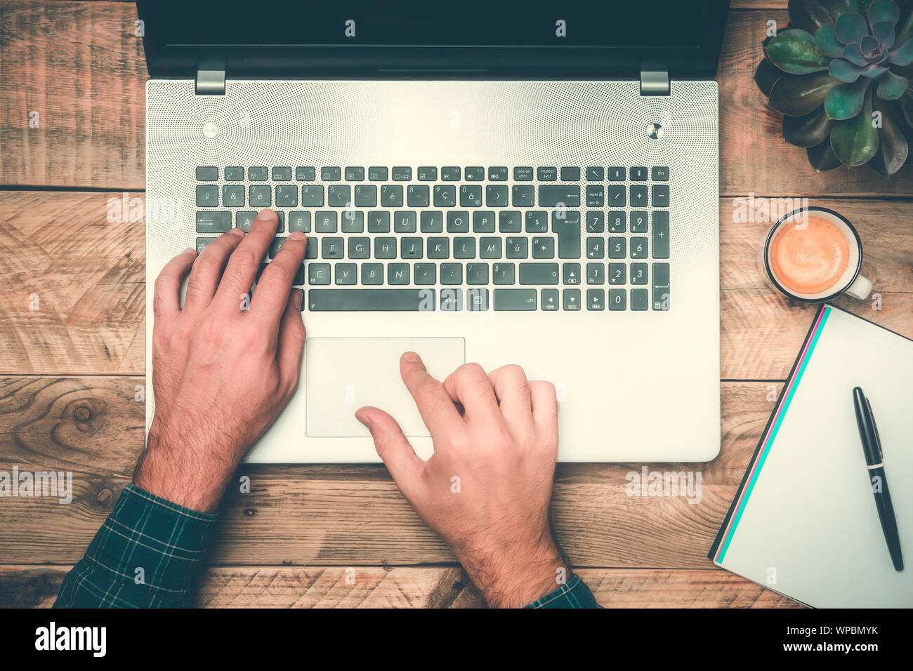 Büro der Ansicht von oben mit den Händen der Texteingabe auf einem Laptop. Rustikalen Holzmöbeln, Schreibtisch mit Computer, Anlage, Kaffee und Notebook. Moderner Arbeitsplatz Konzepte. Stockfoto