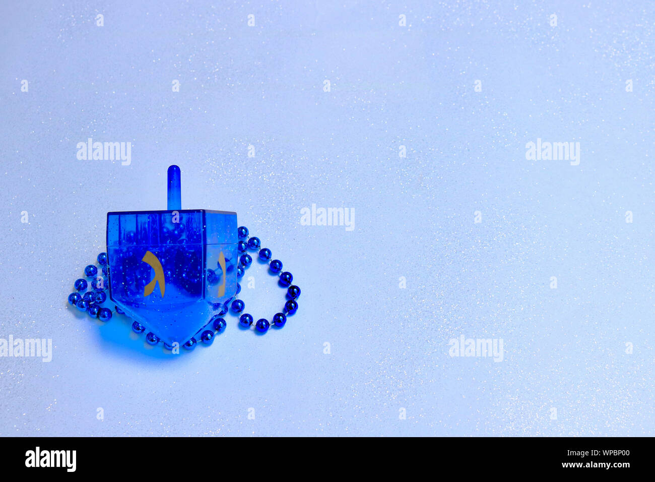 Blau dreidel und Perlen gegen einen hellblauen sparkly Hintergrund Stockfoto