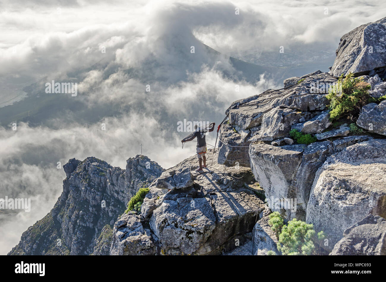 Extremsportler der Vorbereitung seines Haltegurtverankerung an der Table Mountain Plateau auf der atlantischen Seite der Tabelle mit Tiefliegenden Bewölkung über den Lion's Stockfoto