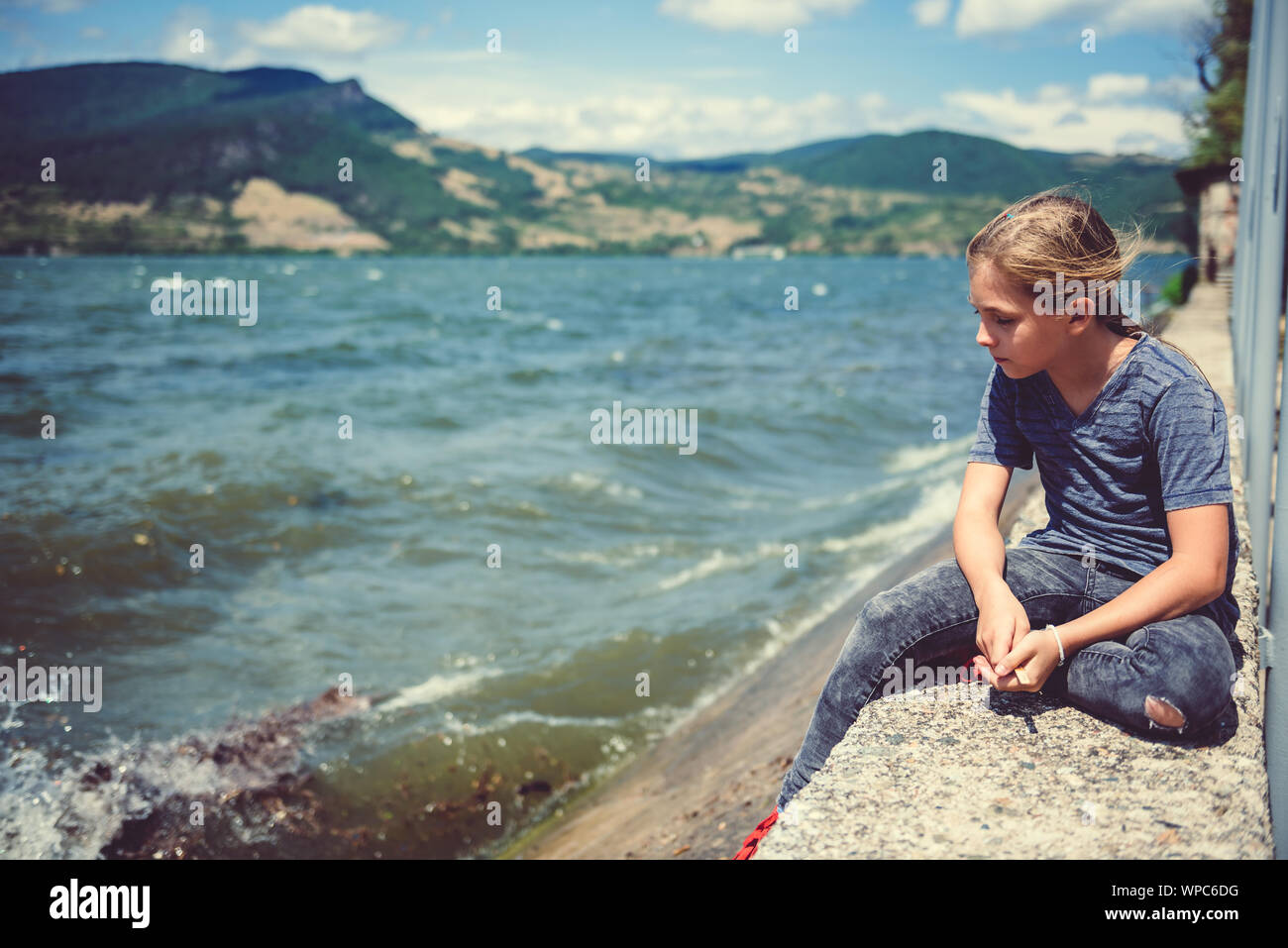 Trauriges kleines Mädchen sitzen durch das Wasser an einem windigen Tag Stockfoto