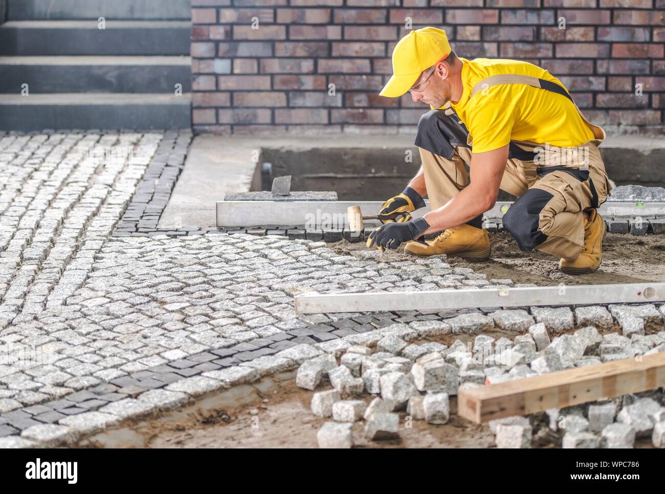 Professionelle kaukasischen Arbeiter Gebäude Granit gepflastert Hardstanding Garten Weg. Industrielle Thema. Stockfoto