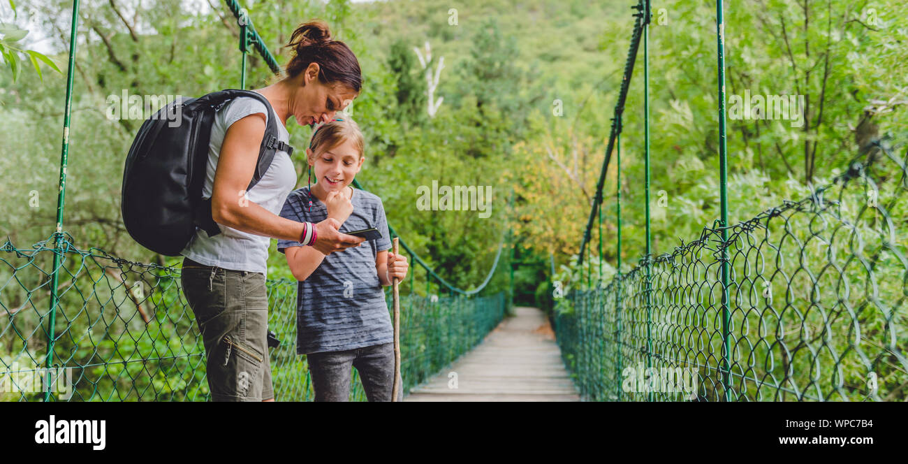 Mutter und Tochter stehen auf hölzerne Hängebrücke in den Wald und mit smart phone zu navigieren. Stockfoto