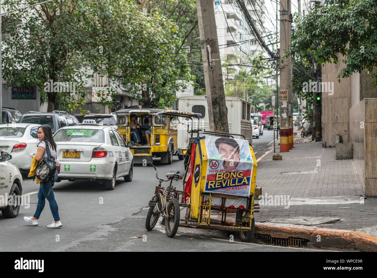 Manila, Philippinen - 5. März 2019: Rot-gelb Dreirad Taxi mit einem großen Plakat der Bong Revilla, Schauspieler und Politiker in der Straße mit Autos, grau buildi Stockfoto