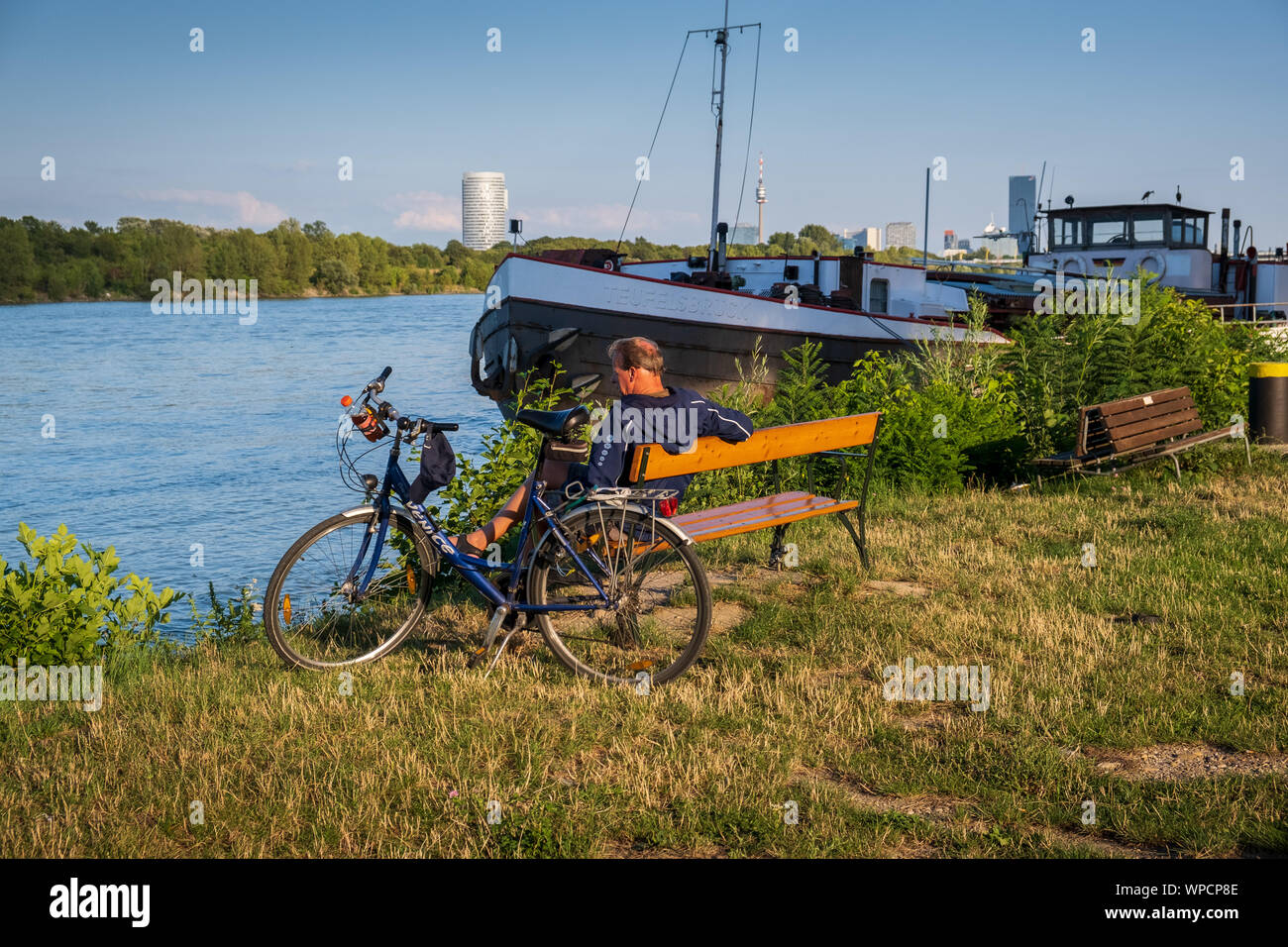 Wien, Österreich - 14 August 2019: ein Radfahrer ruht auf einer Bank neben der Donau. Stockfoto