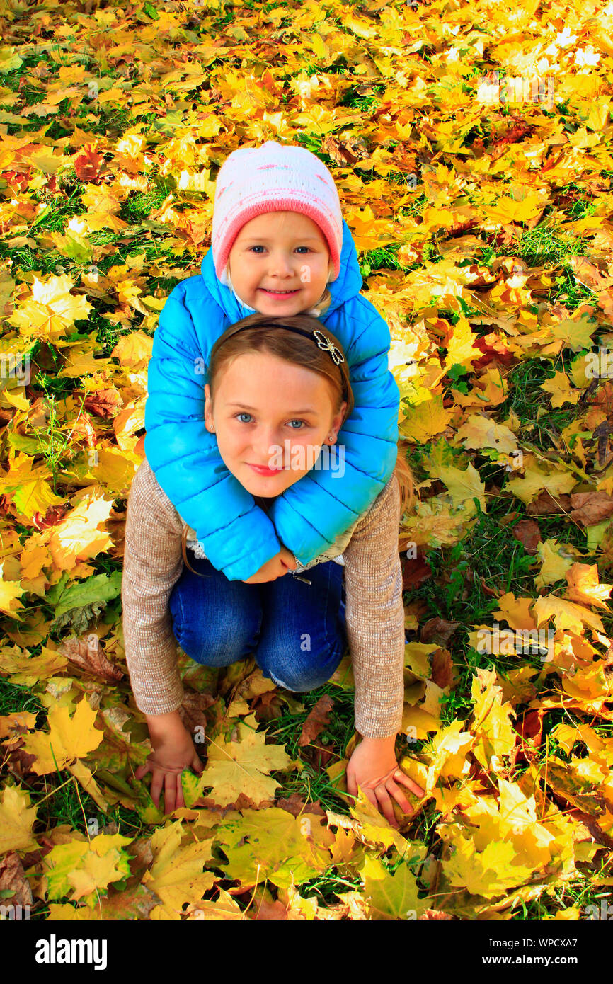 Junge hübsche Schwestern sitzen und auf gelben Blätter im Herbst Park umfassen. Kleine Kinder mit Blätter im Herbst. Kleine Mädchen im Herbst Wald. Herbstliche Stimmung. Ein Stockfoto