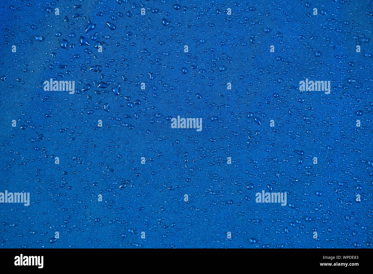 Anzeigen Textur blau Synthetische wasserdichte Kleidung. Wasser auf wasserdichte Nylon fällt. Regen fällt auf Wasserabweisendem Textil. Wasserdichte Beschichtung Hintergrund Stockfoto
