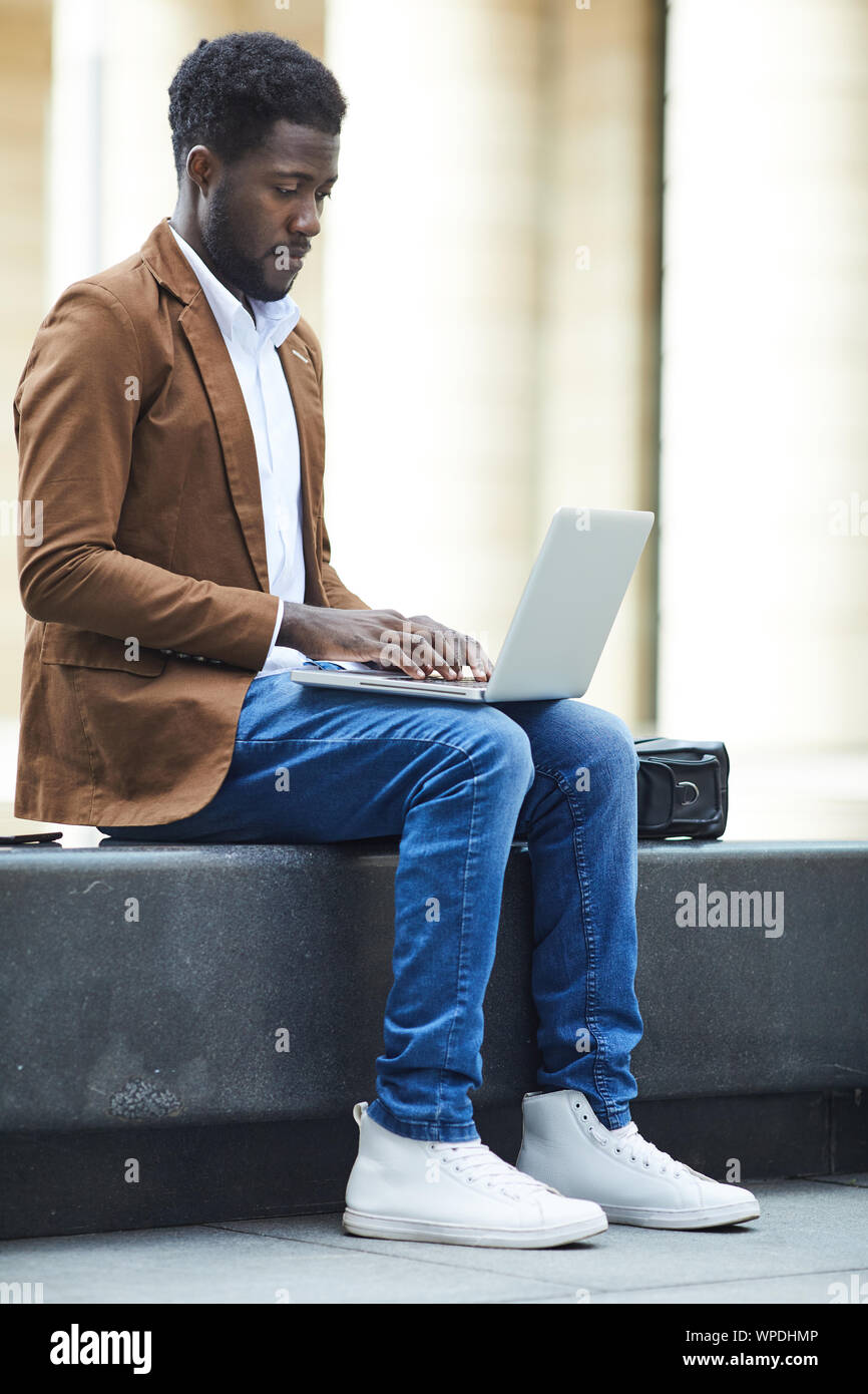 Volle Länge seitliche Ansicht der jungen Afrikaner - Mann mit Laptop im Freien während auf freiberufliche Projekt im urbanen Umfeld arbeiten, kopieren Raum Stockfoto