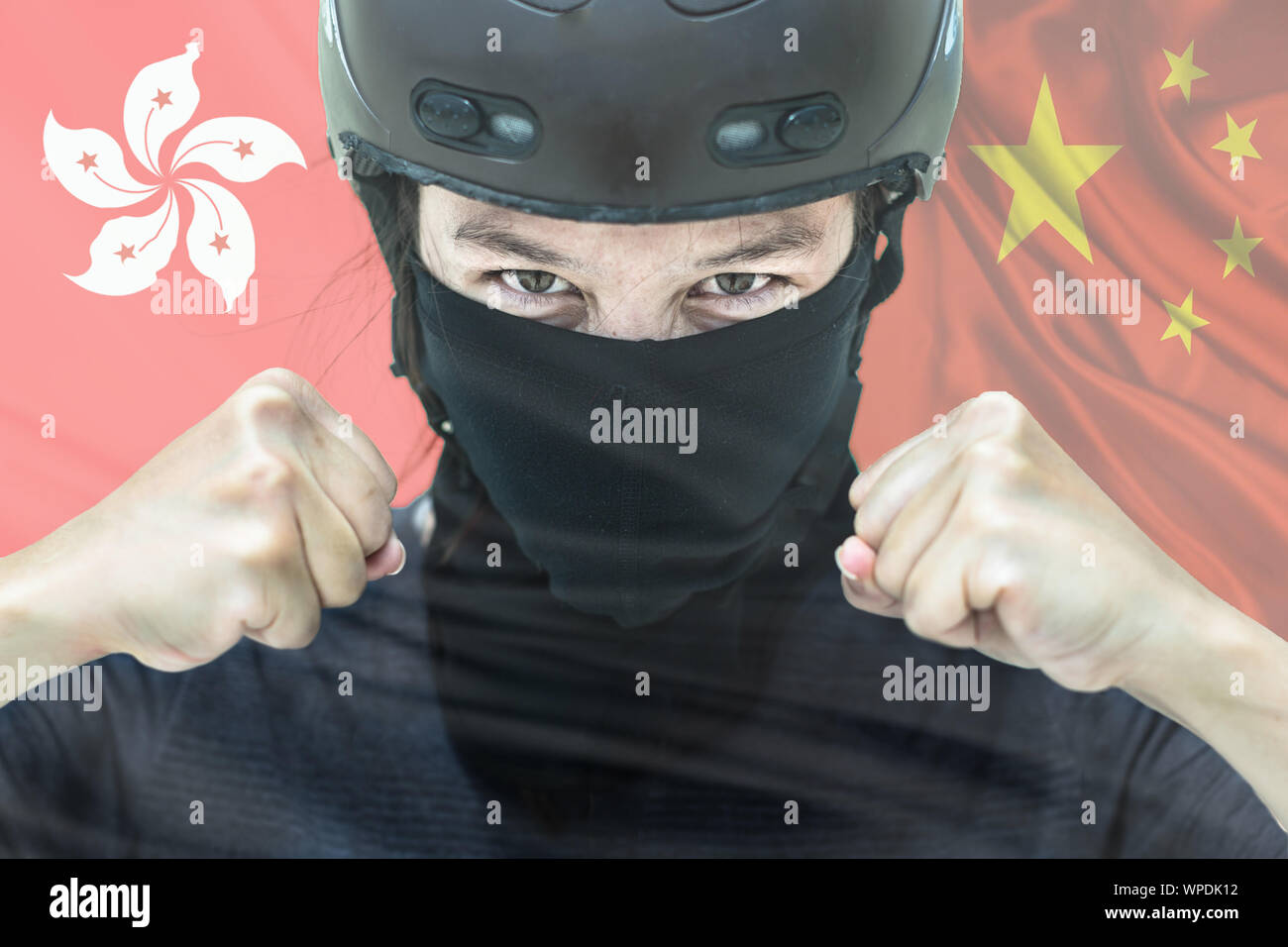 Das Porträt einer Demonstrant in Kampfausrüstung mit der Hong Kong und chinesischen Flaggen im Hintergrund Stockfoto