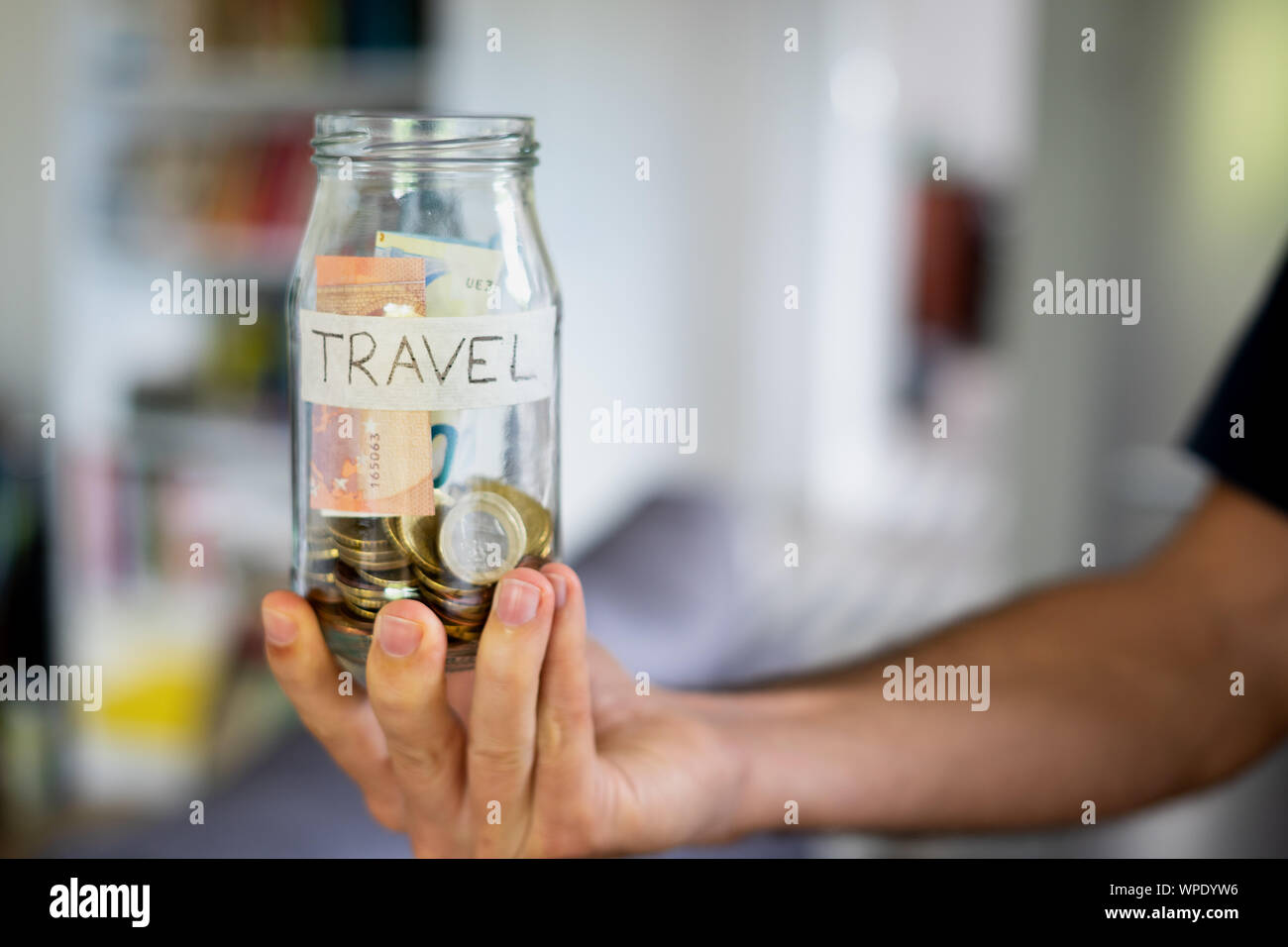 Des Menschen Hand ein Glas mit Euro-Münzen und -Banknoten und einen handgeschriebenen Etikett sagen reisen. Stockfoto