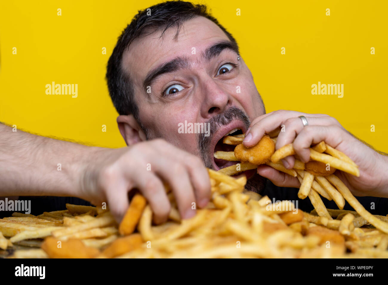 Essen der Trödelnahrung Ernährung und diätetischen Gesundheit Problem Konzept. Junger Mann essen mit beiden Händen eine sehr große Menge ungesundes fast food. Diät Versuchung r Stockfoto