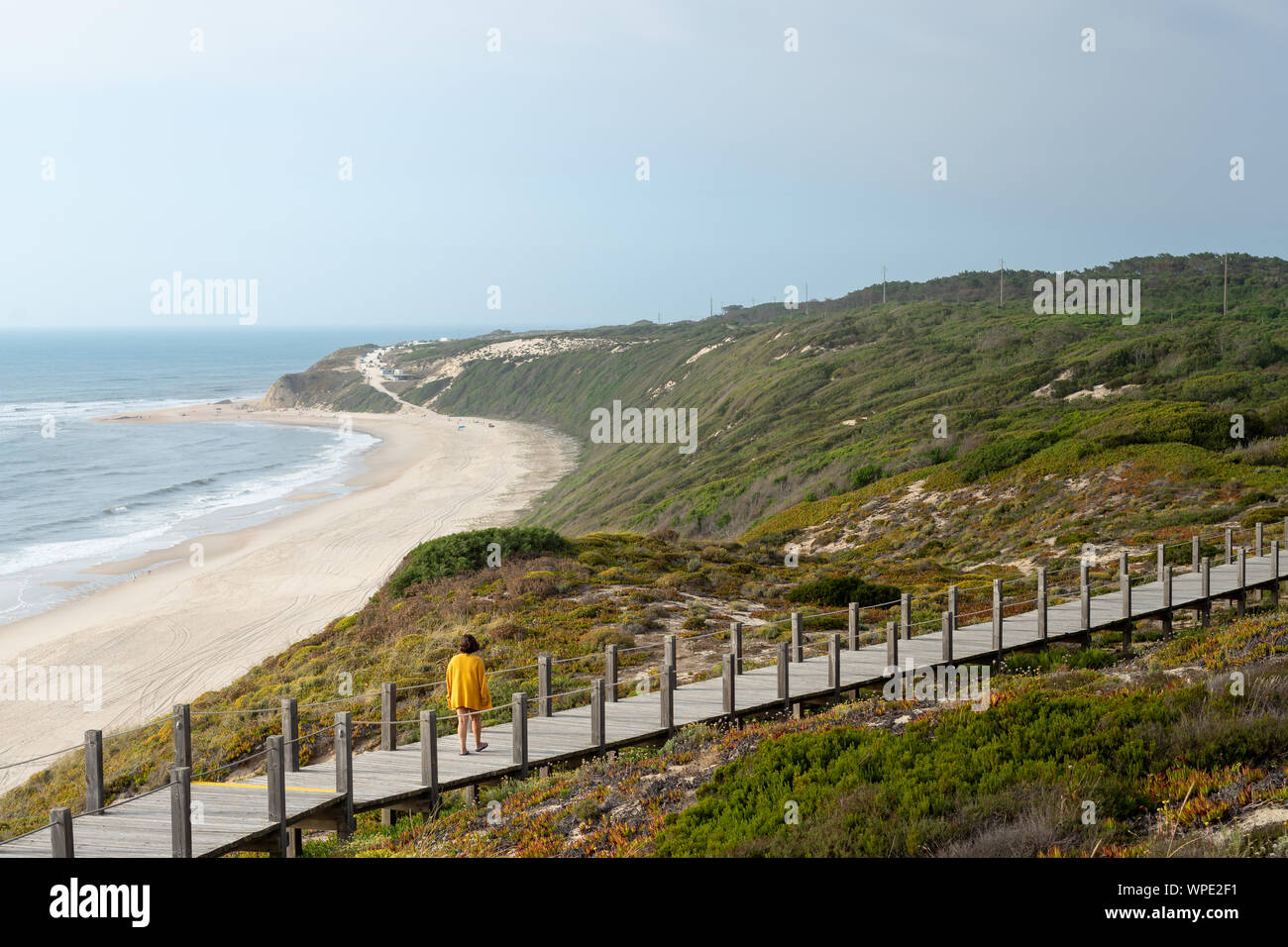 Mädchen in einem Abstand in einer langen Holzsteg mit Blick auf den Strand. Durch die Vegetation und das Meer umgeben. Stockfoto