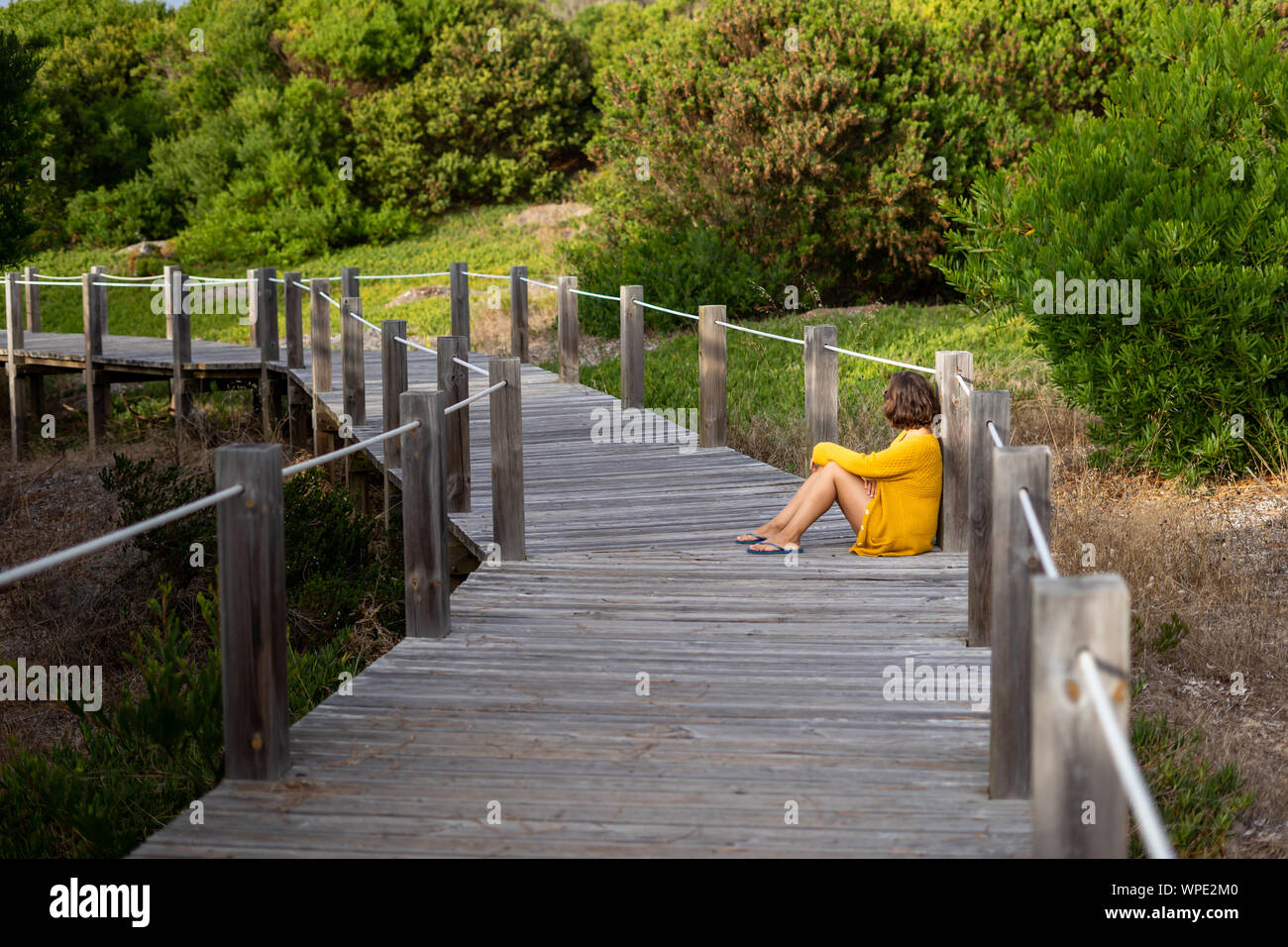 Eine junge Frau in einem Abstand sitzen auf dem Boden eines Holz- weg von der Natur umgeben. Stockfoto