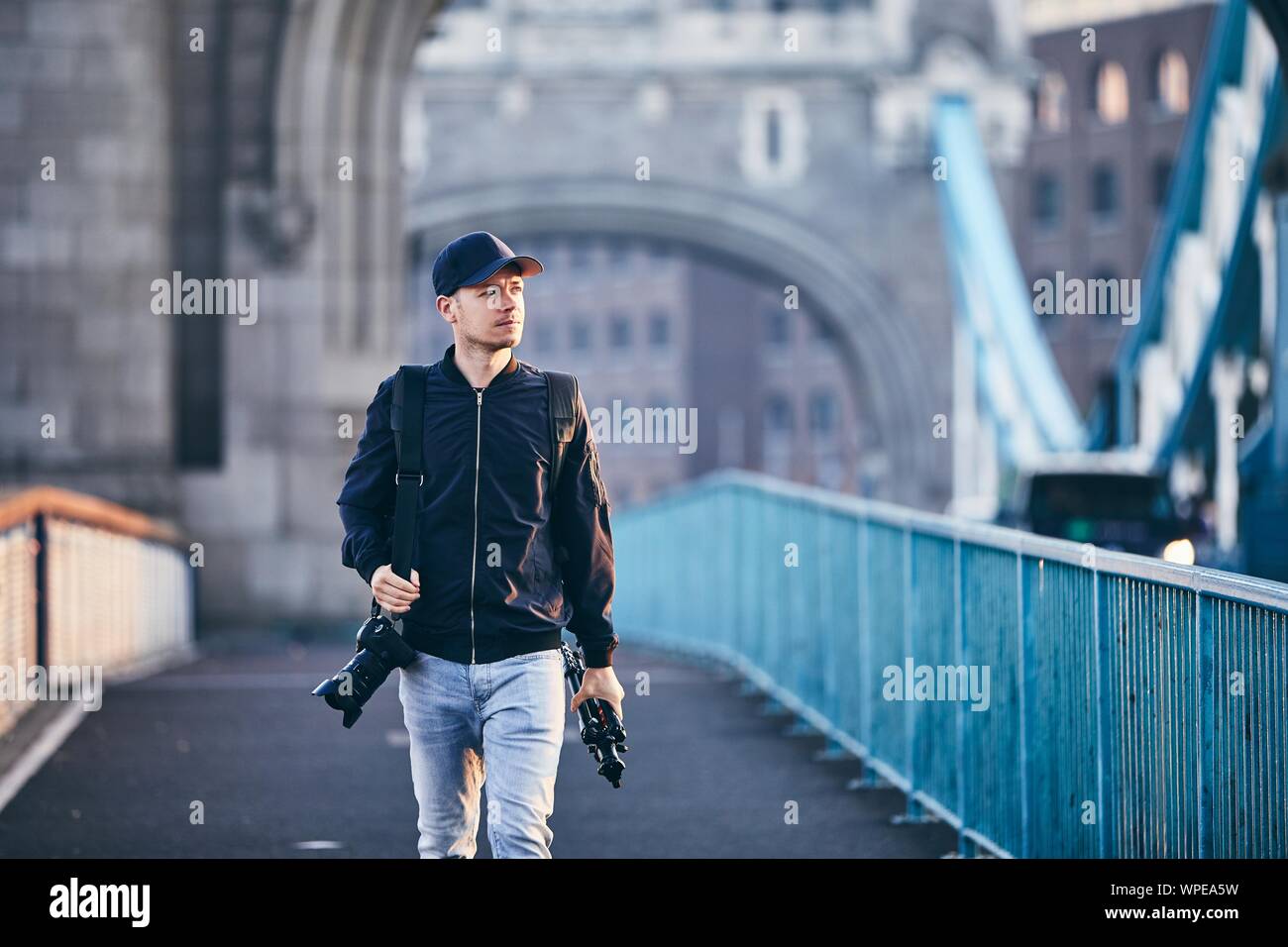 Fotograf weg schauen, beim Tragen von Kamera und Stativ gegen die Tower Bridge. London, Vereinigtes Königreich. Stockfoto