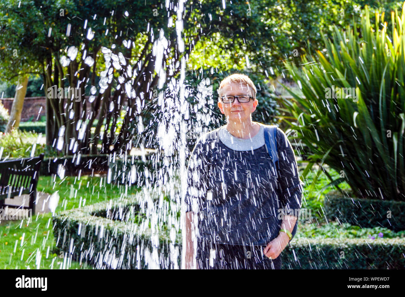 Eine Frau Brille hinter ein Brunnen steht in einem Park an einem Sommertag, London, UK Stockfoto