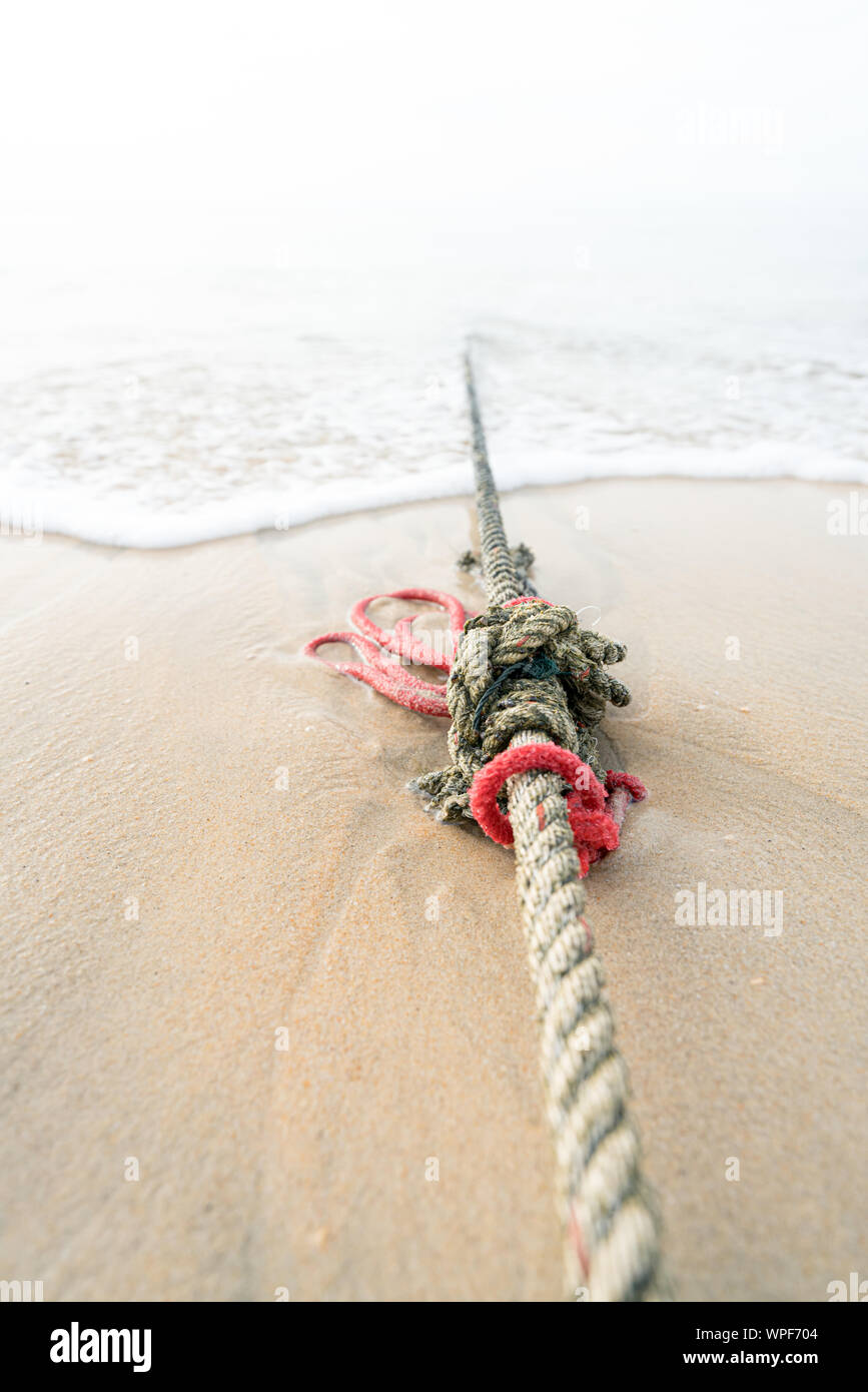 Kreative rote Seil geknotet Schiffe liegen auf einem Sandstrand, die auf das Meer an der Küste wie die Flut kommt. Stockfoto