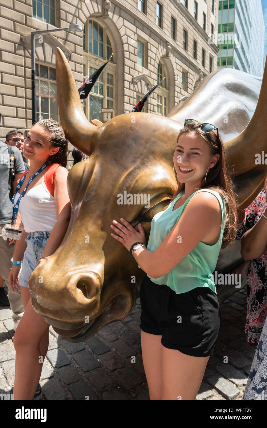 New York Bull, Ansicht von zwei jungen Frauen fotografiert neben dem wütenden Stier Skulptur in Broadway, Manhattan, New York City, USA stationiert werden Stockfoto