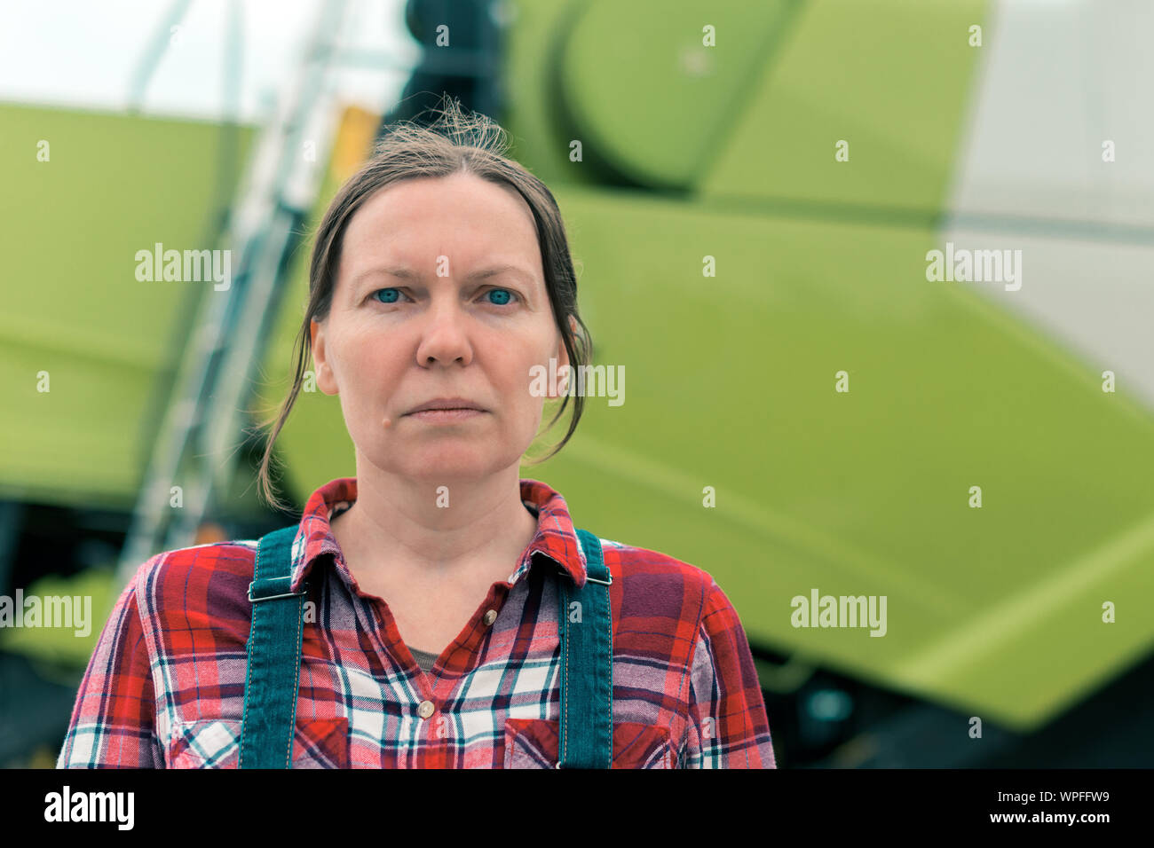 Frau Bauer in der Vorderseite des Mähdreschers posieren. Ernsthafte Frau Landarbeiter mit landwirtschaftlichen Maschinen bereit, die Ernte. Stockfoto
