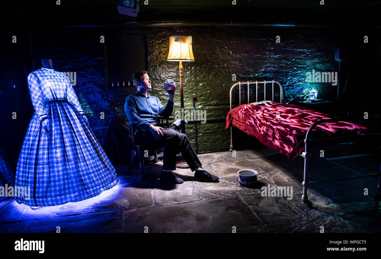 Museum Mitarbeiter Harry Jelley hält das Modell eines Auges, als Objekte um ihn herum werden durch Licht von Projektoren Teil der Wie Mein Licht ist für die Installation von Frank Cottrell-Boyce am Bronte Parsonage Museum in Haworth, West Yorkshire zu bilden. Stockfoto