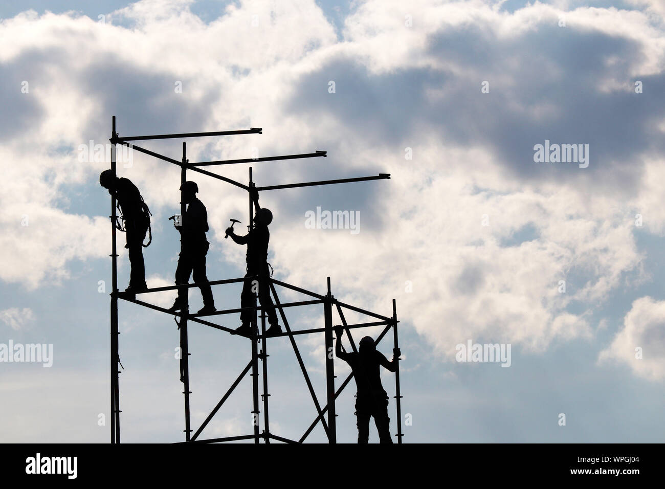 Bauarbeiter auf Gerüsten. Silhouetten, die Arbeiten auf der Baustelle gegen den blauen Himmel mit weißen Wolken Stockfoto