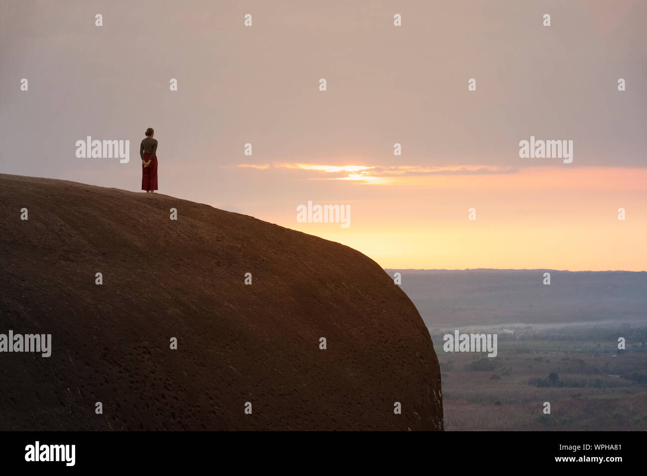 Frau, die auf einer Klippe mit Sonnenuntergang und Sonnenaufgang Hintergrund Stockfoto