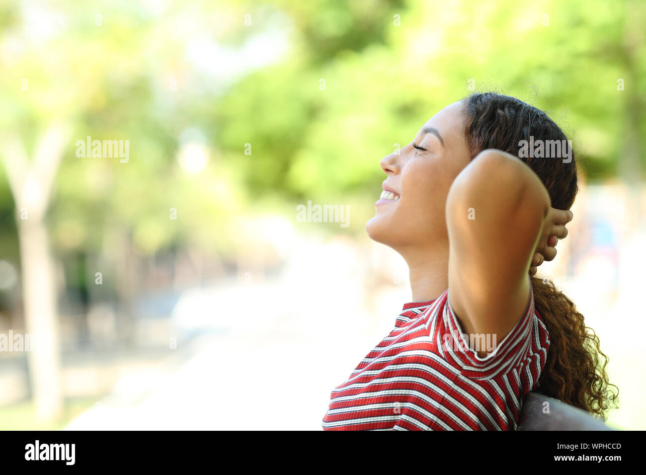 Seitenansicht Portrait Of Happy gemischten Rasse Frau ruhend sitzen auf einer Bank in einem Park Stockfoto