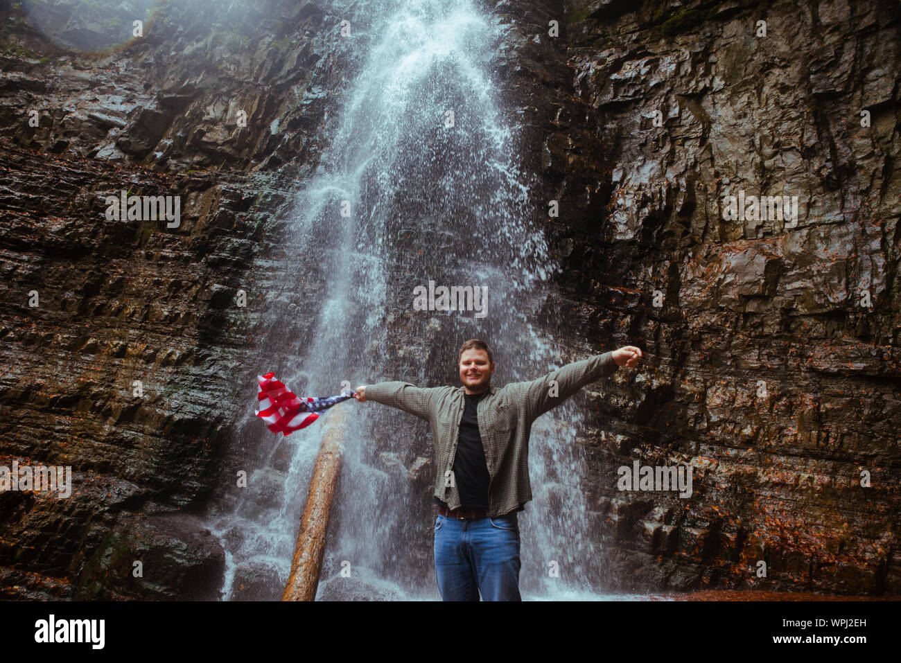 Mann mit USA-Flagge Wasserfall im Hintergrund Stockfoto