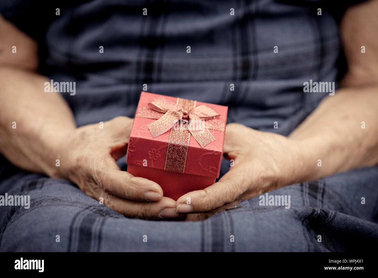 Zerknitterte alte Hände halten kleines Geschenk mit roter Schleife, AF, Oldtimer und Classic Chrome Tone. Stockfoto