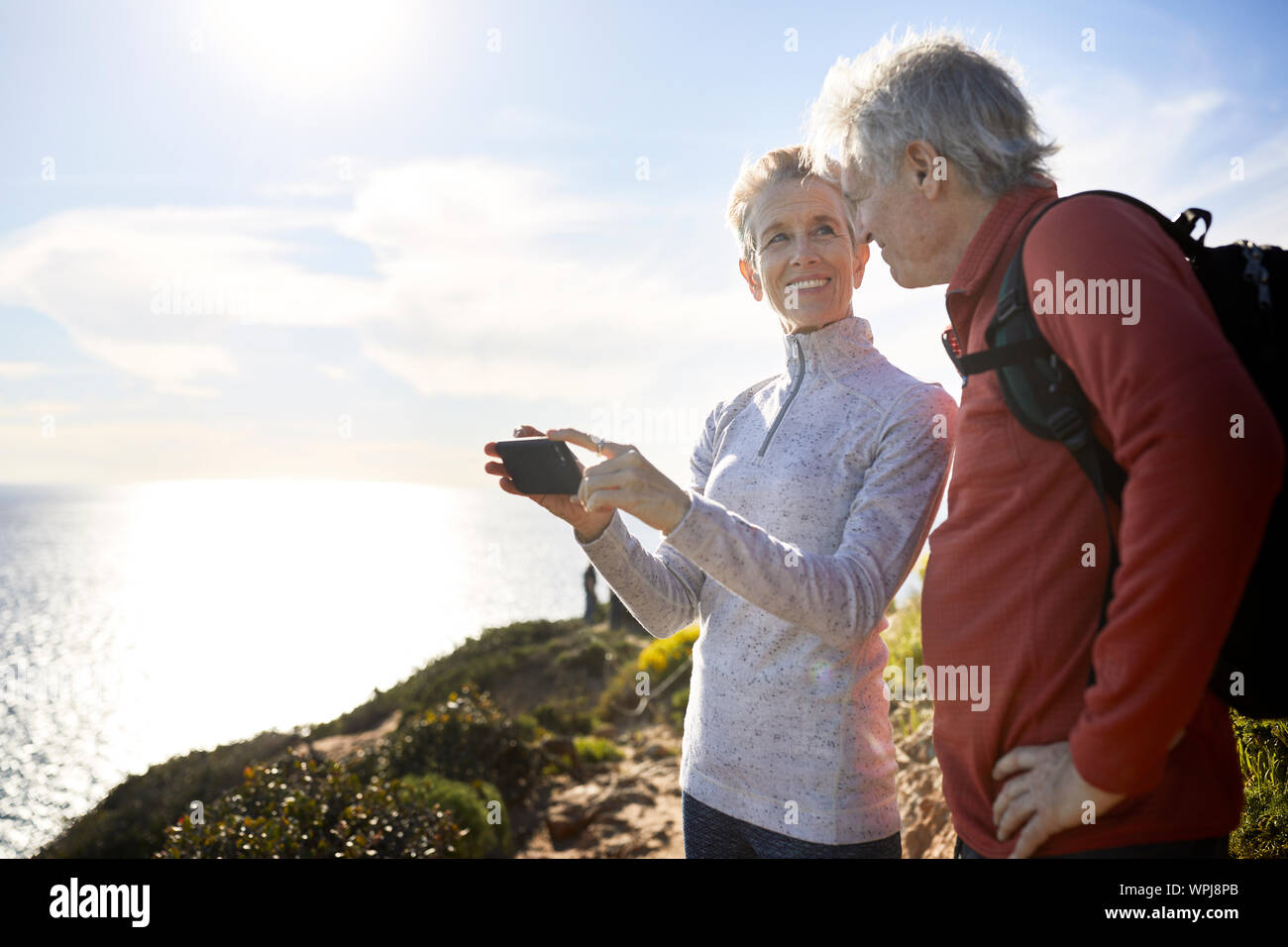 Lächelnde ältere Frau auf der Suche nach Mann, während Sie smart phone gegen Sky Stockfoto