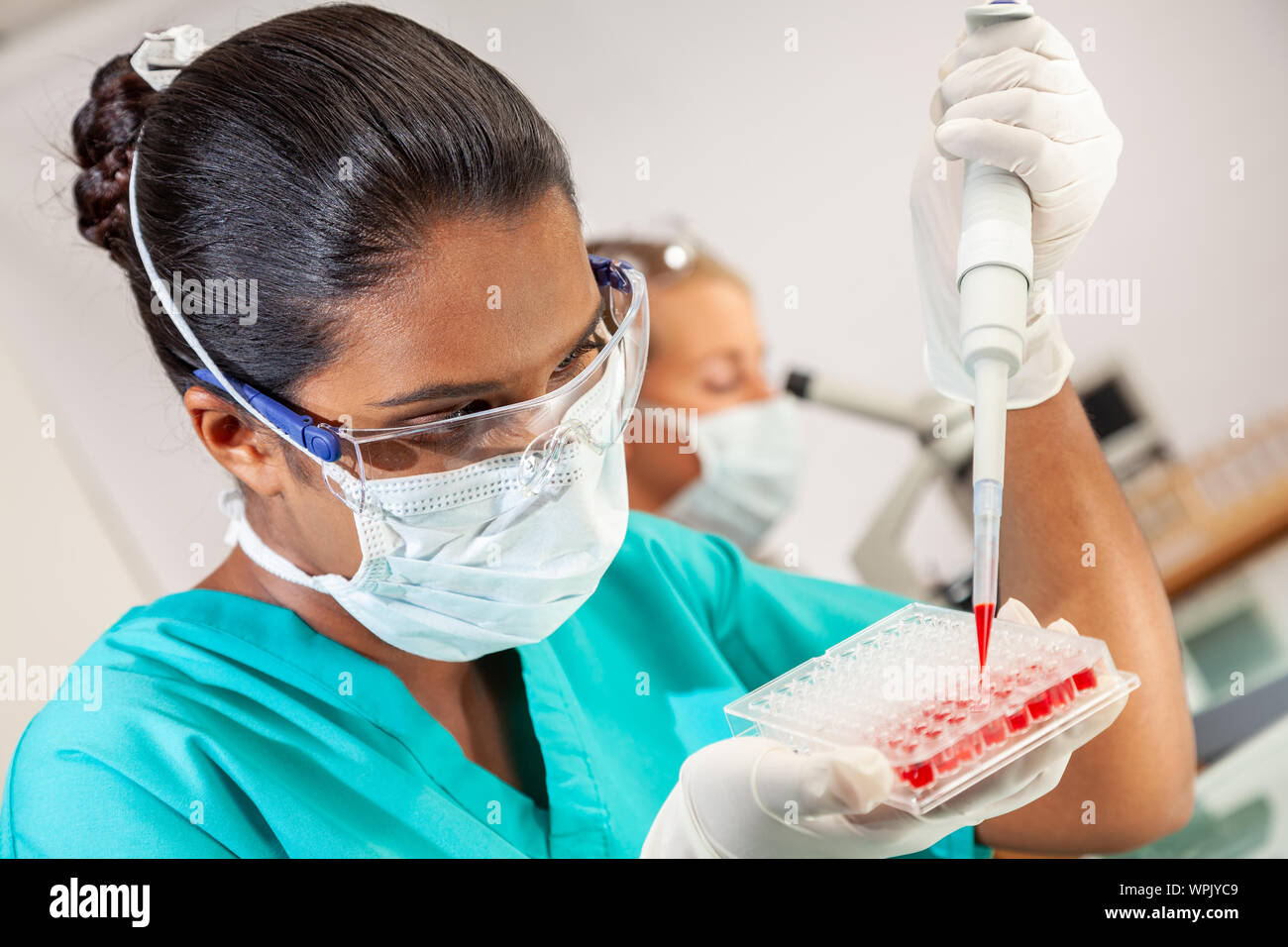 Weibliche Asiatische medizinische oder wissenschaftliche Forscher oder Arzt mit einer Pipette und Sample fach Blutprobe in einem Labor mit Frau Kollegin zu testen Stockfoto