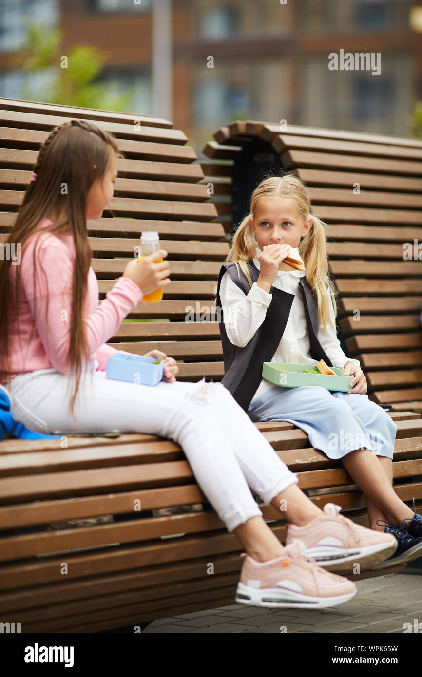 Zwei Freunde essen Sandwiches und Saft trinken, während Sie auf der Bank sitzen zusammen im Freien während der Schulferien Stockfoto