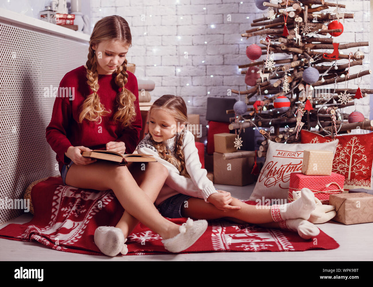 Mädchen Schwester Freunde umarmen sitzen am Weihnachtsbaum, das Konzept der Kindheit, Weihnachten und Neujahr, auf hellem Hintergrund Stockfoto