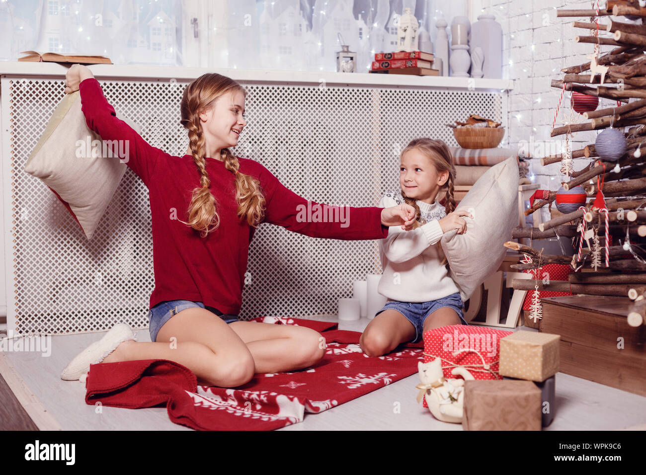 Mädchen Schwester Freunde umarmen sitzen am Weihnachtsbaum, das Konzept der Kindheit, Weihnachten und Neujahr, auf hellem Hintergrund Stockfoto