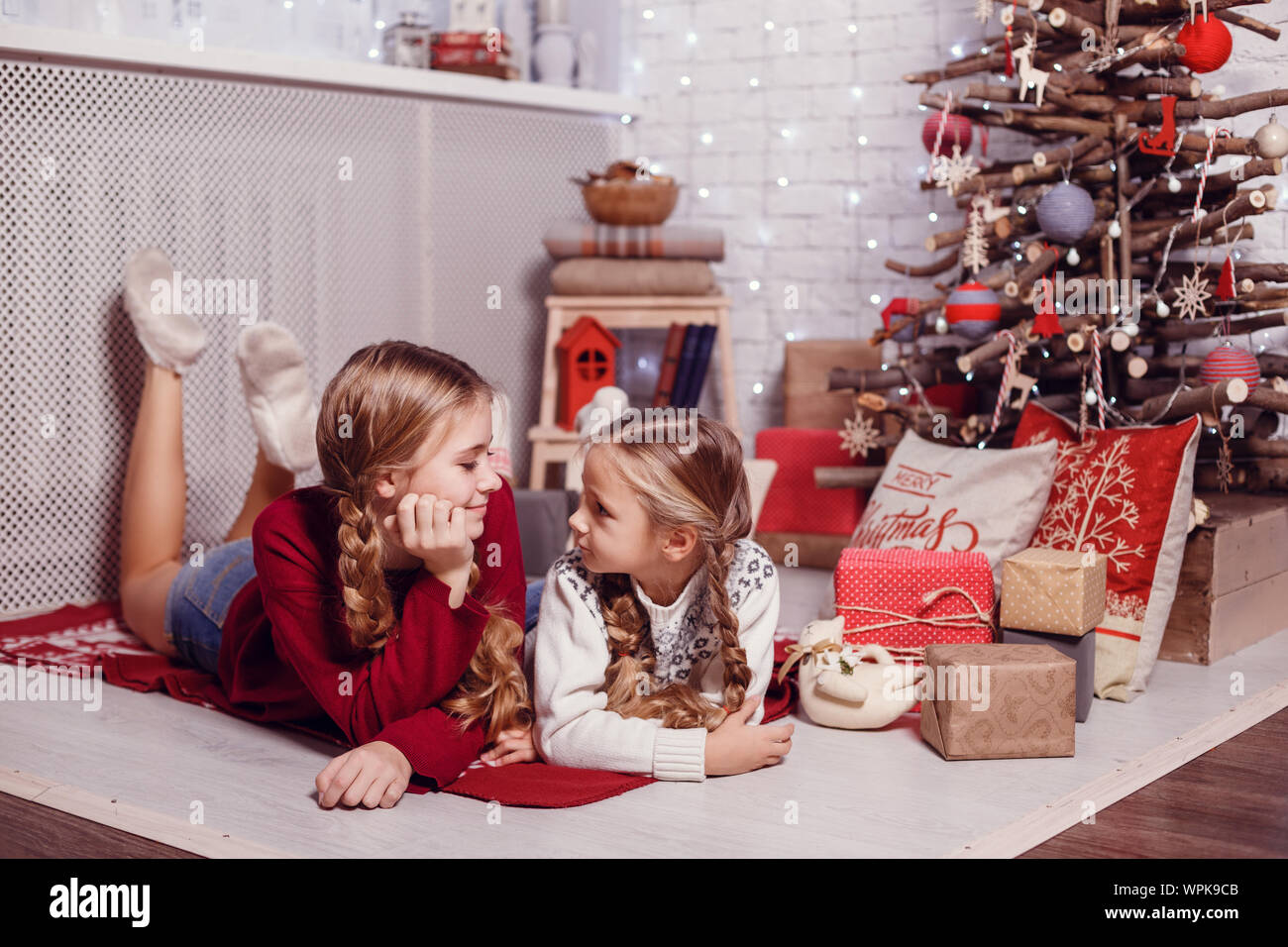 Mädchen Schwester Freunde umarmen sitzen am Weihnachtsbaum, das Konzept der Kindheit, Weihnachten und Neujahr, auf hellem Hintergrund Stockfoto