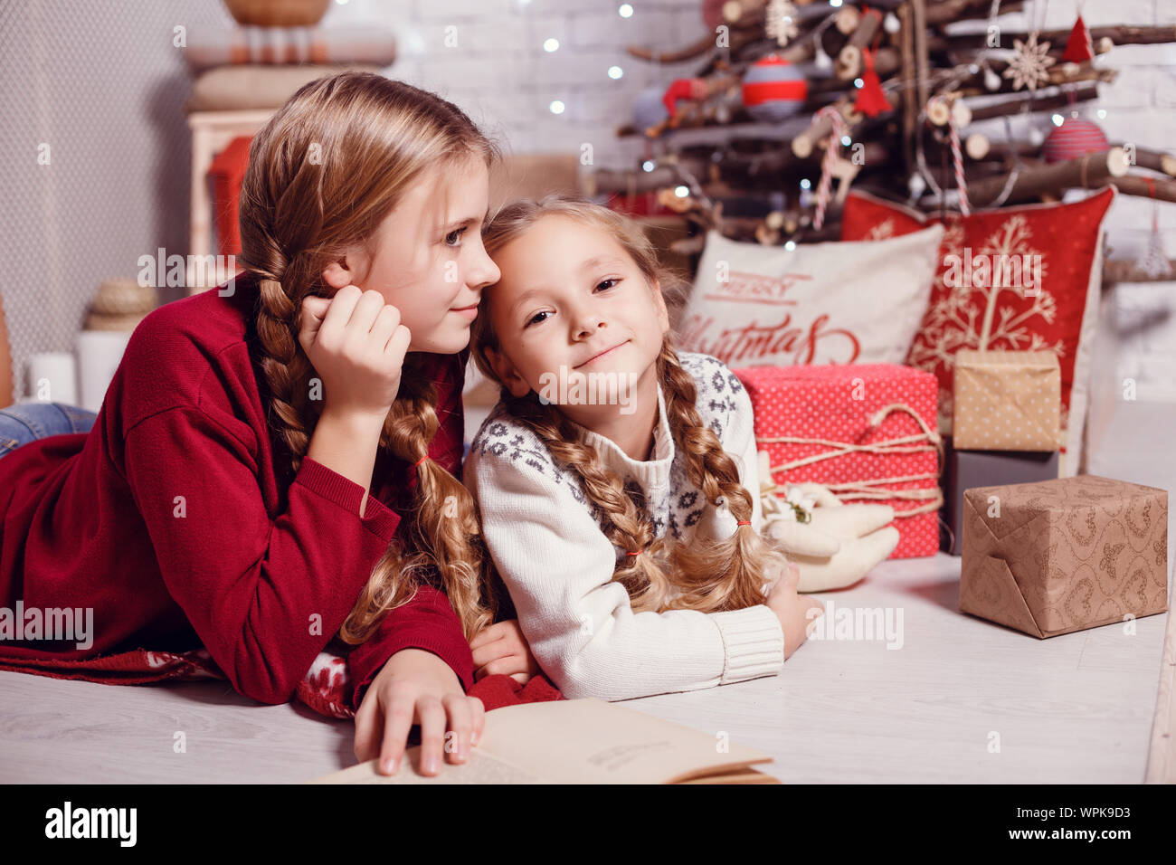 Mädchen Schwester Freunde umarmen sitzen am Weihnachtsbaum, das Konzept der Kindheit, Weihnachten und Neujahr, auf hellem Hintergrund Stockfoto