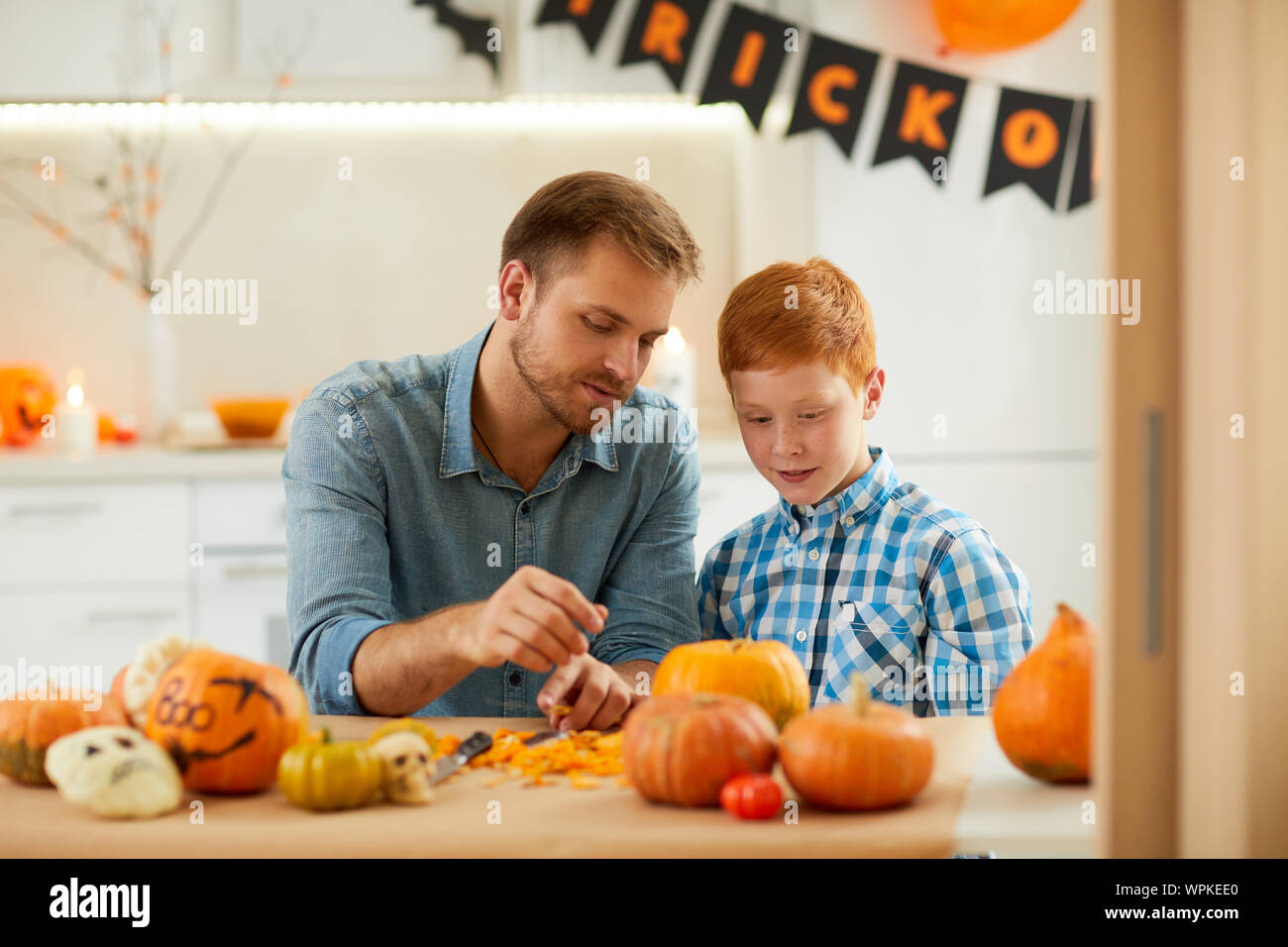 Junger Vater am Tisch sitzen zusammen mit seinem Sohn und Sie Jack O'Lantern für Halloween Stockfoto