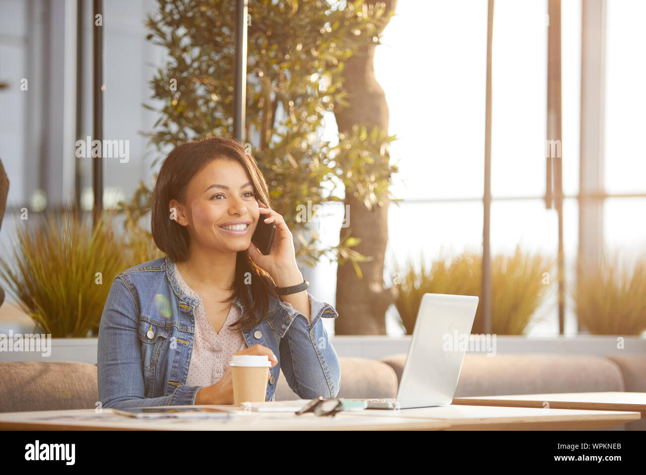 Afrikanischer junge geschäftsfrau Gespräch am Handy und lächelnd, während am Tisch vor Laptop im Café sitzen Stockfoto